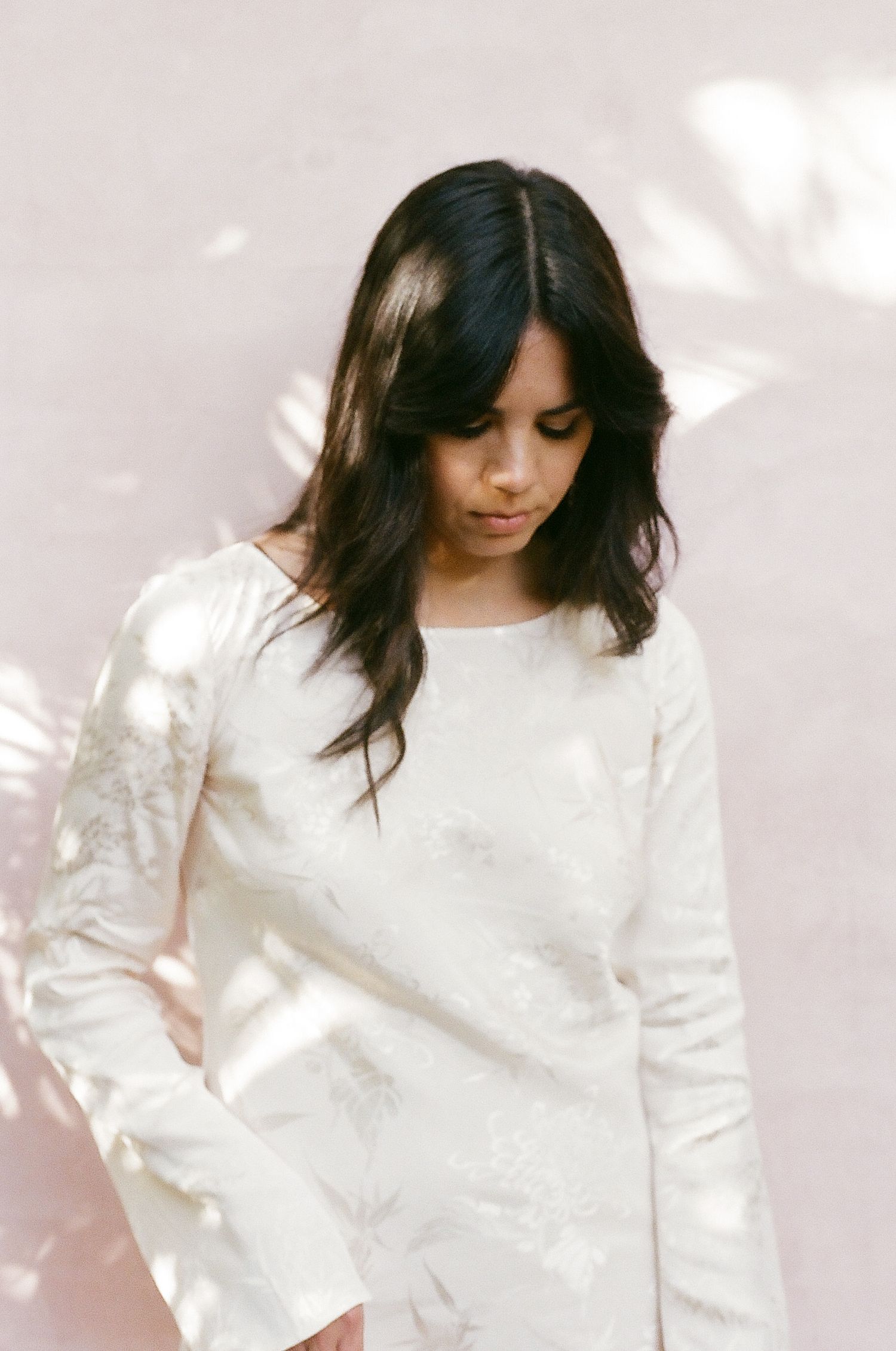 Person wearing white long sleeve dress in soft, dreamy lighting with flowing hair.