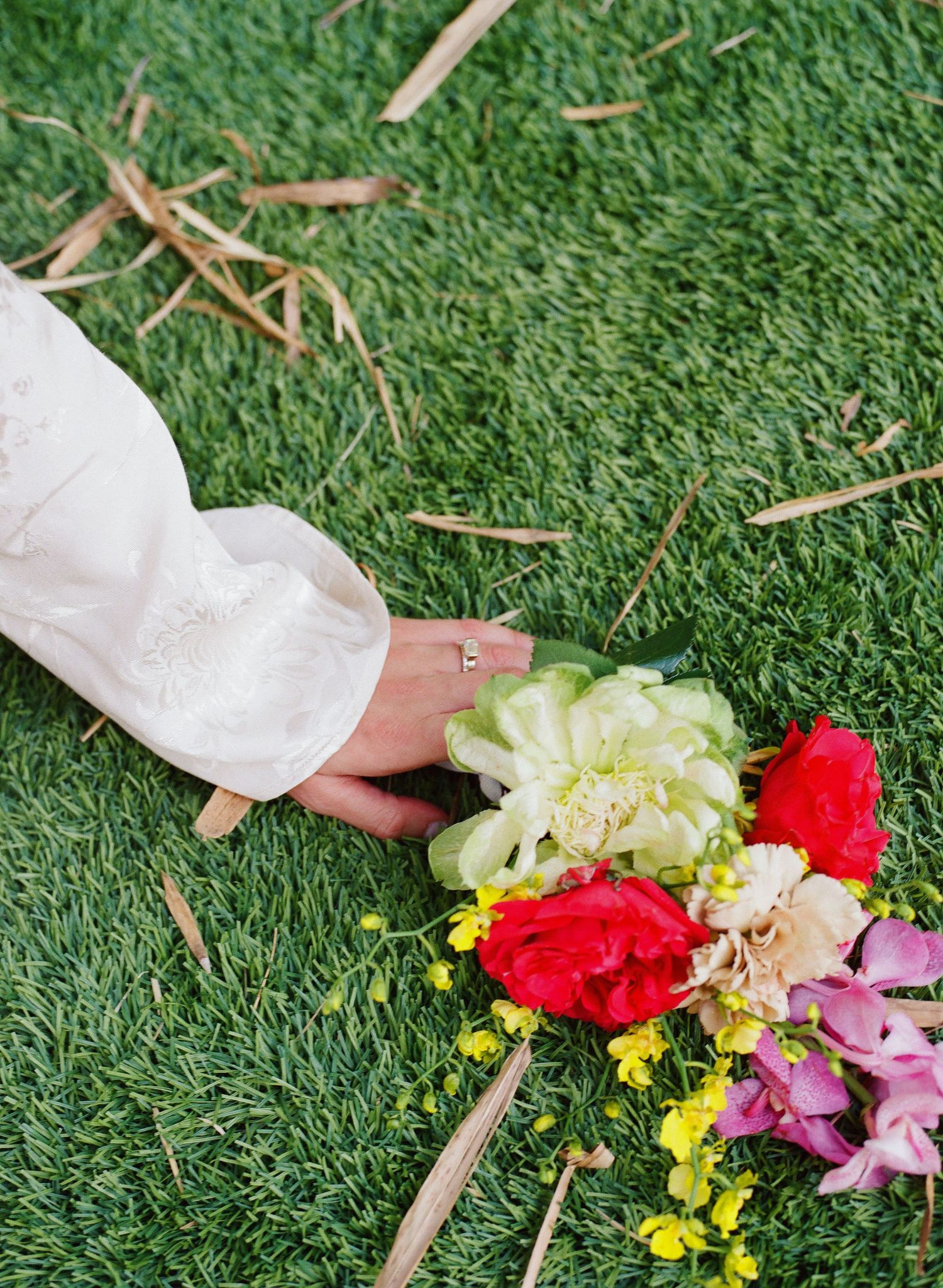 Colorful flowers including red carnations and yellow blooms arranged on green grass.