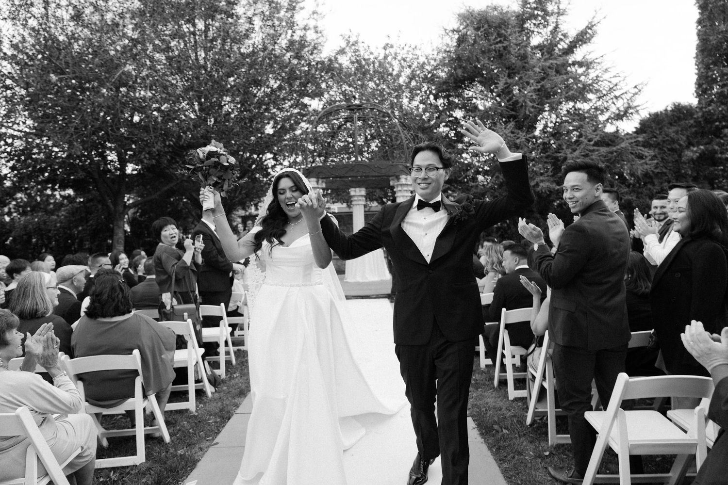An outdoor wedding ceremony with white chairs set up on a lawn surrounded by trees.