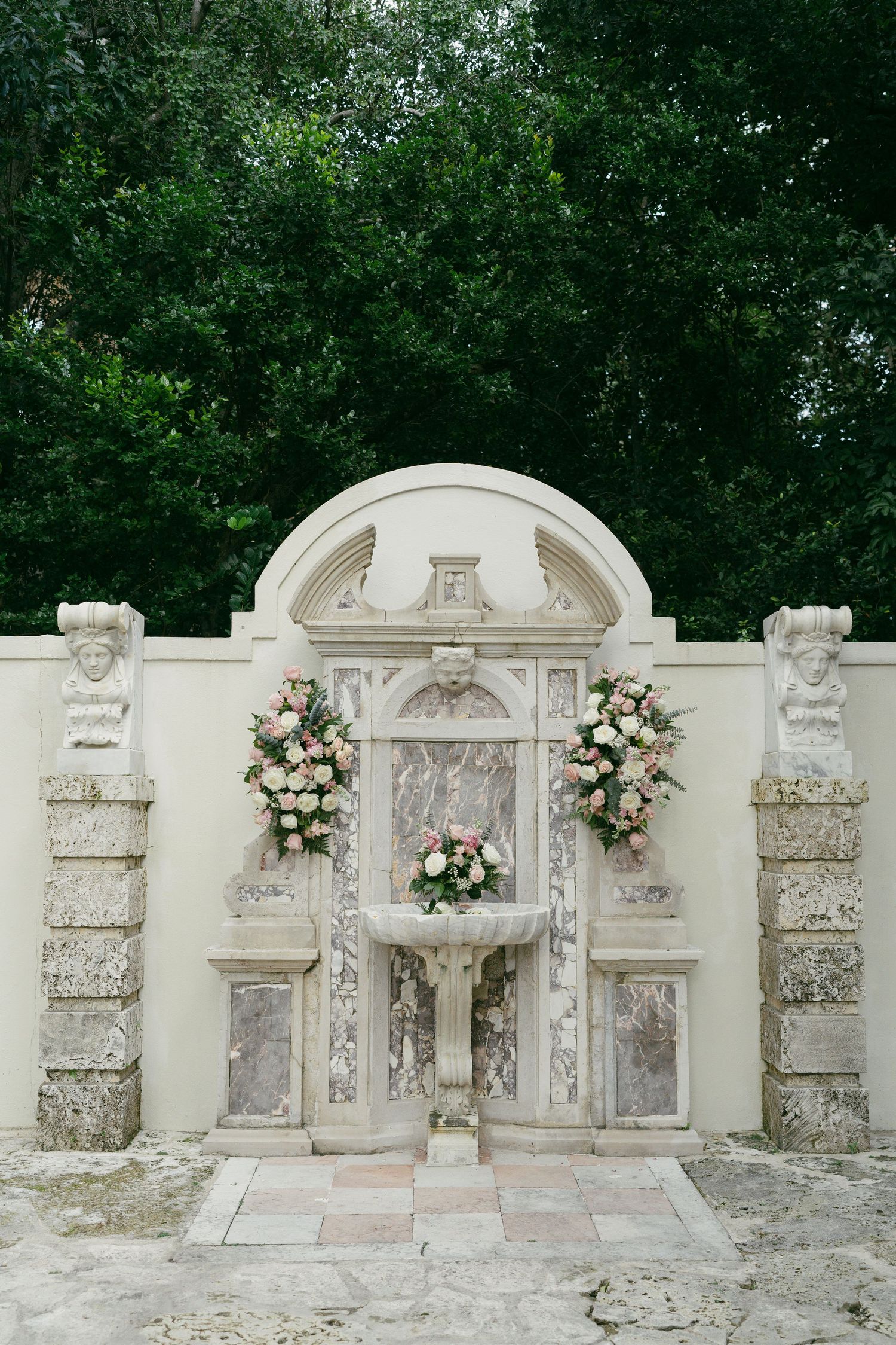 A panoramic view of ornate white stone wall niches decorated with floral arrangements in an outdoor garden setting.