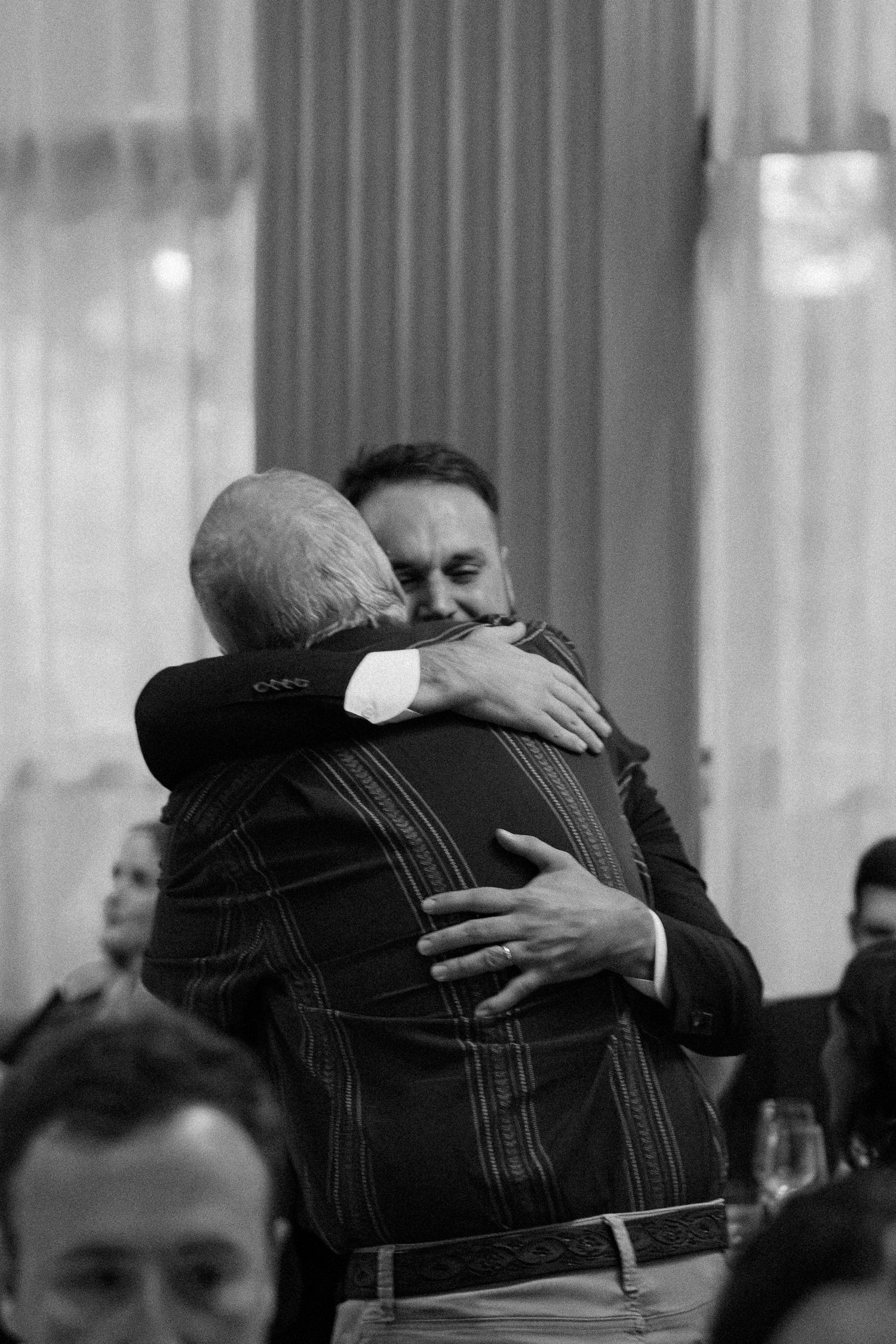People sharing emotional embraces at a formal gathering in black and white.