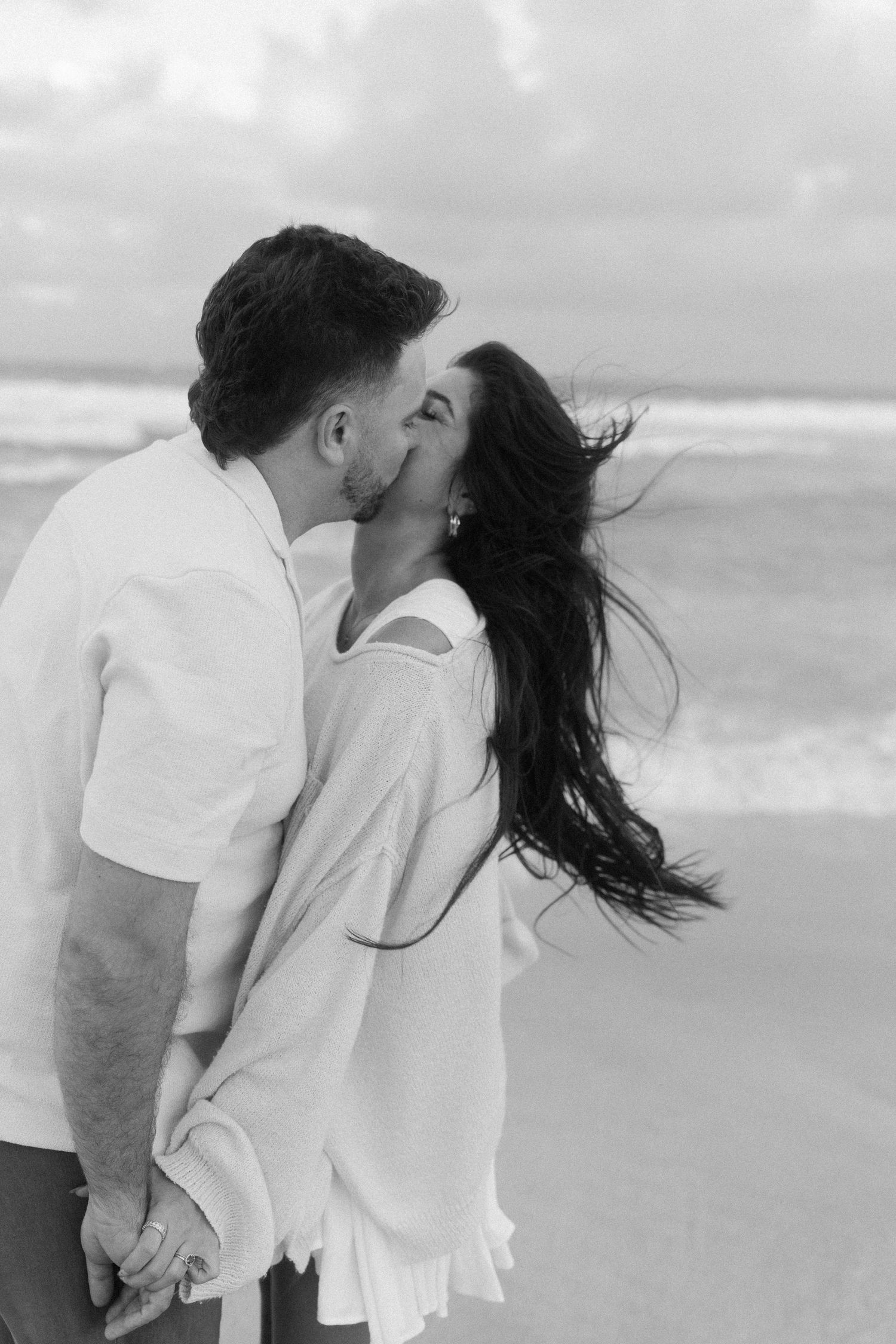 A romantic black and white photo series of a couple embracing and kissing on a windy beach.