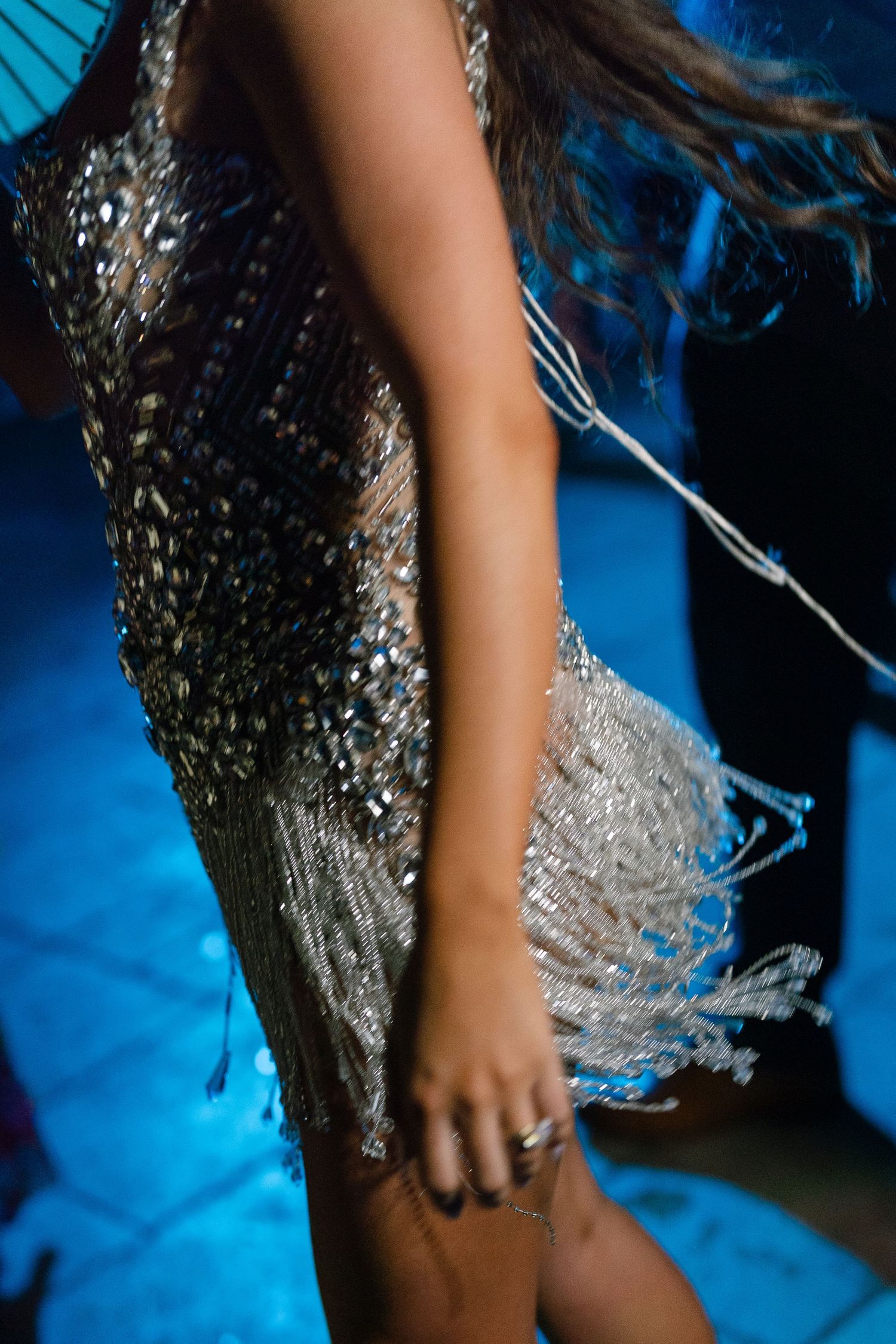 Woman in sparkling silver sequin dress dancing under blue lights at elegant wedding reception.