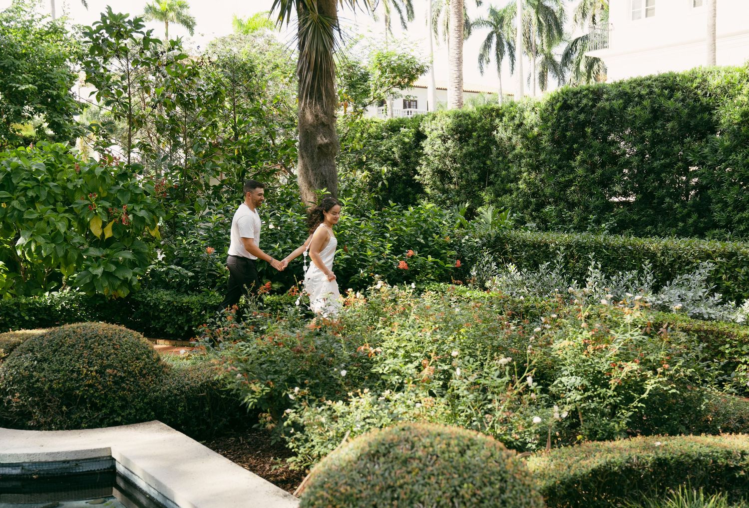 A long public garden path with tropical palm trees and lush landscaping leads through beautiful manicured grounds.