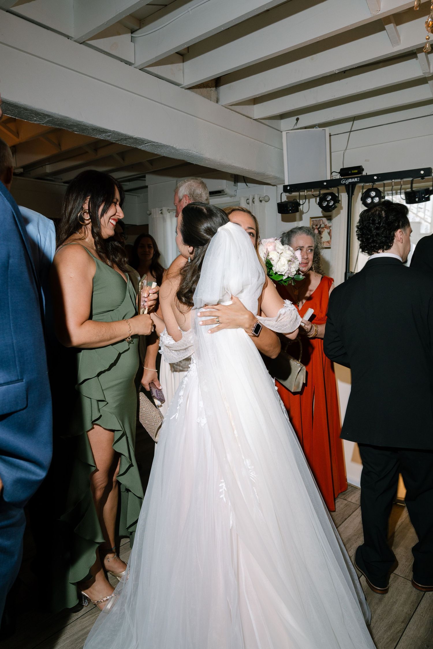 Bride in a white tulle gown embraces a guest during a lively indoor wedding reception.