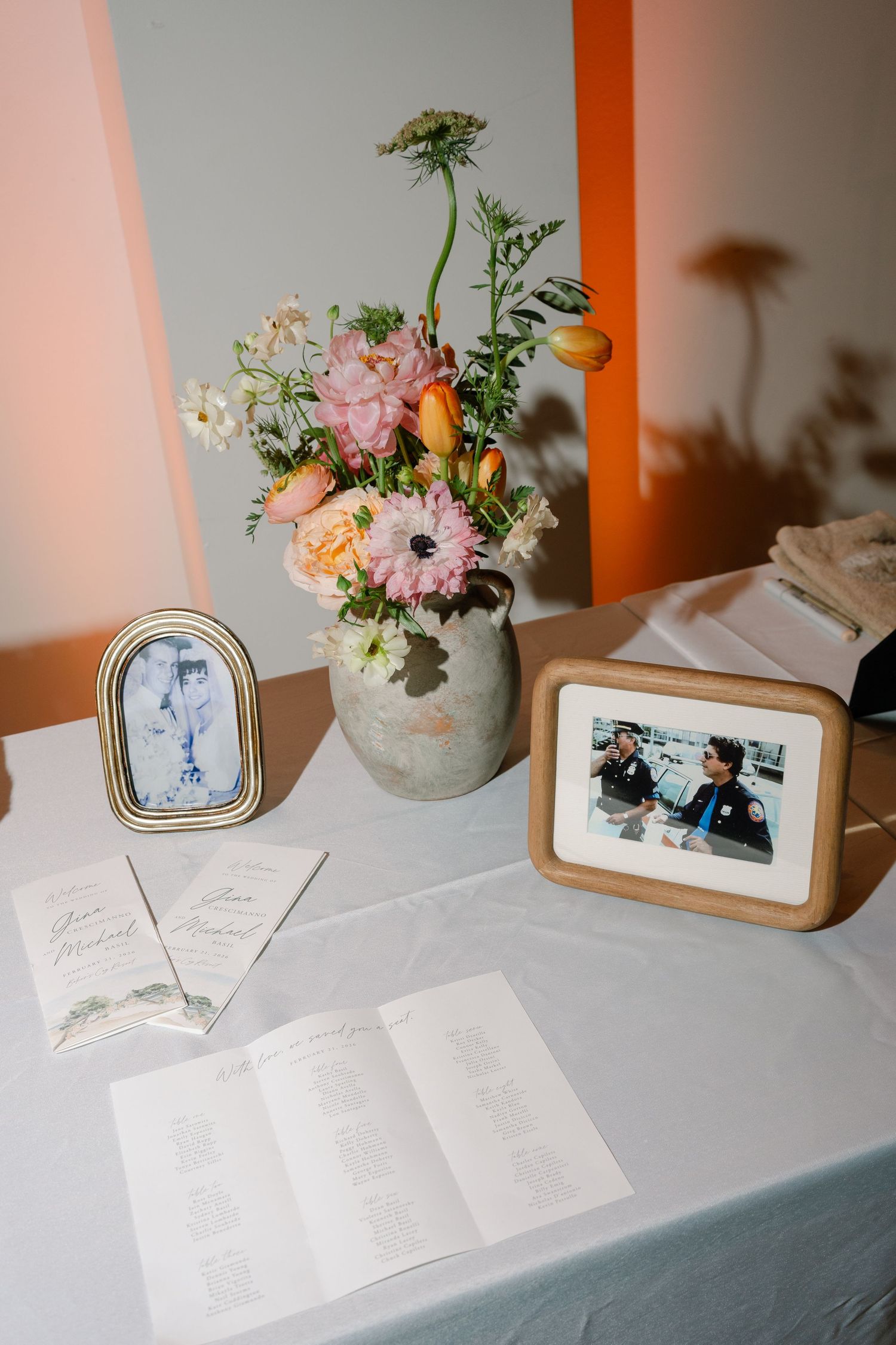 A floral arrangement in a vase sits on a table with framed photos and paper documents.