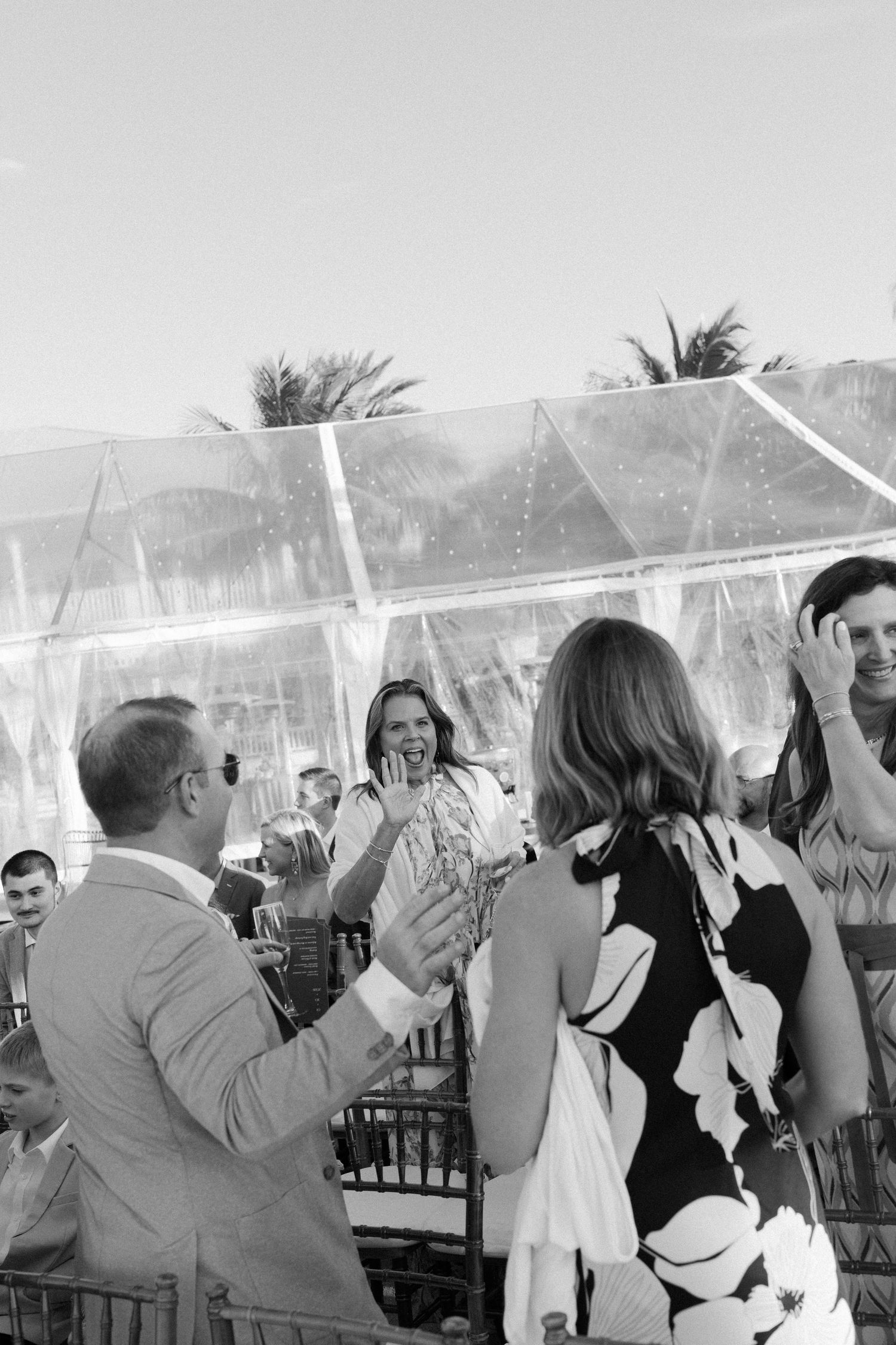 Wedding guests celebrate under a clear tent at an outdoor reception.