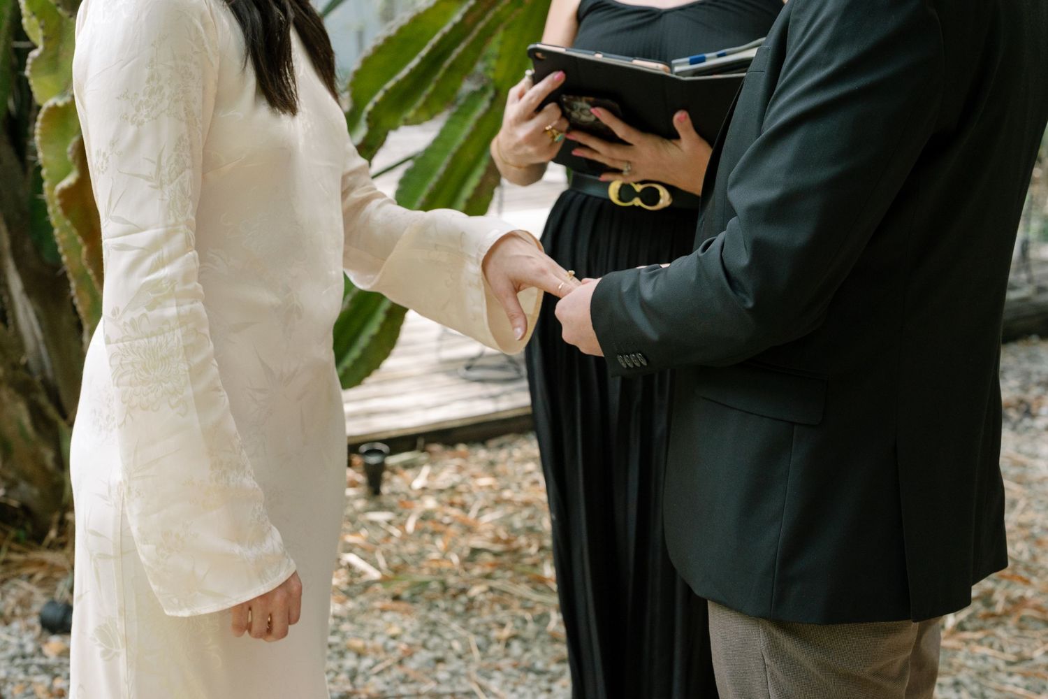 Wedding ceremony in progress with guests seated outdoors under tall trees.