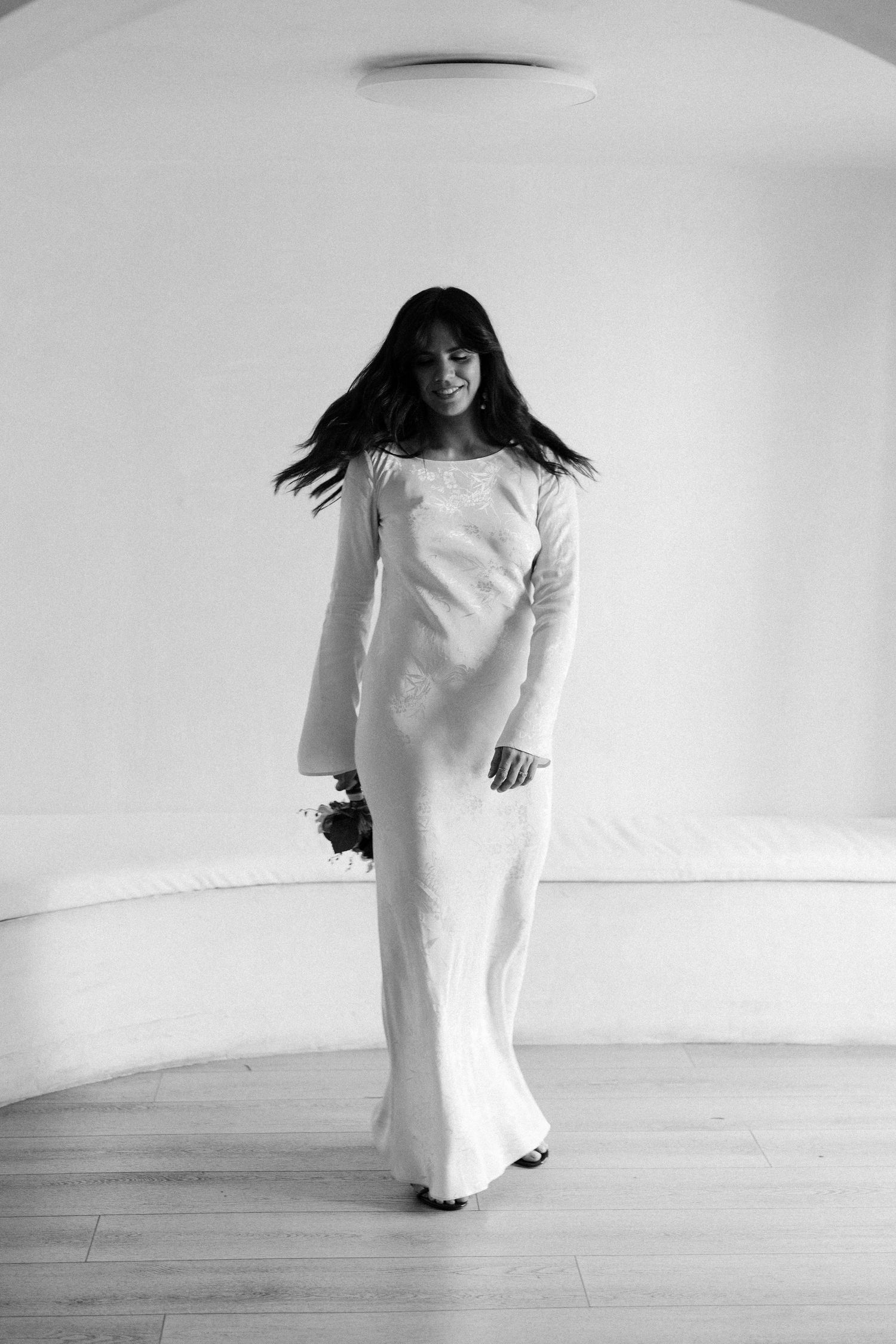 Figure in flowing white dress moves dynamically against minimalist white background.