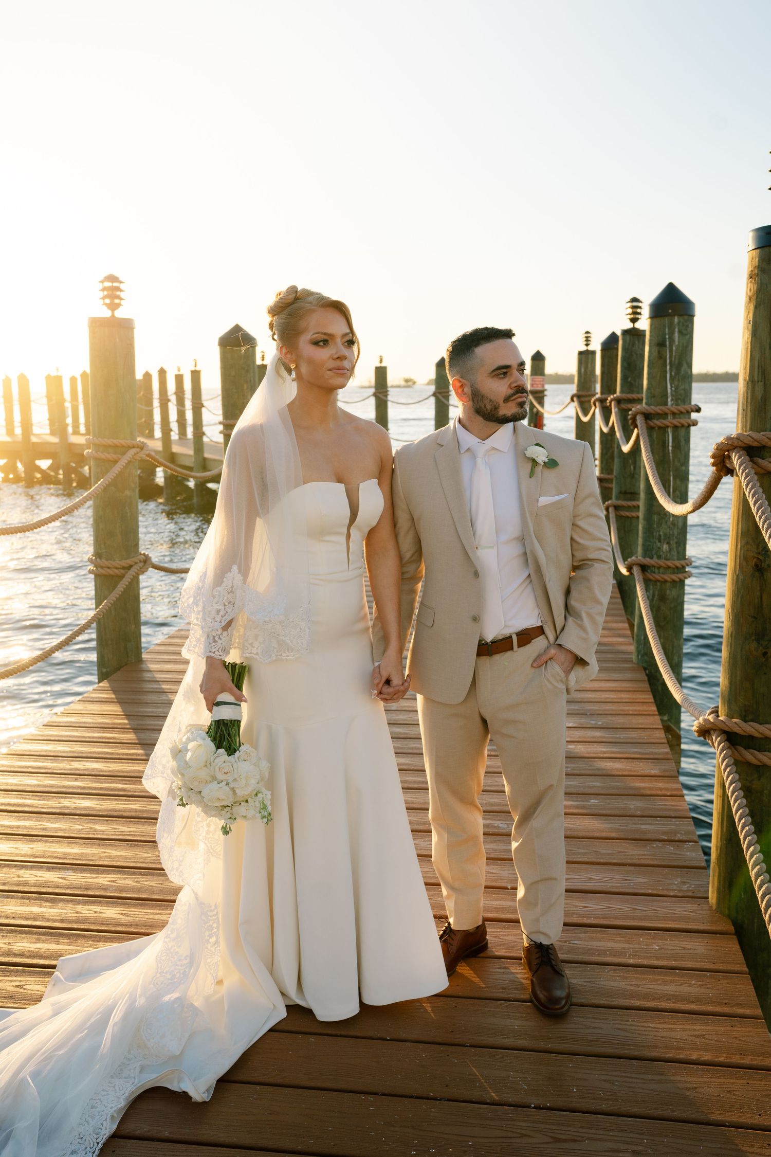 Wedding couple walks along a wooden pier at sunset near the water with their wedding party.