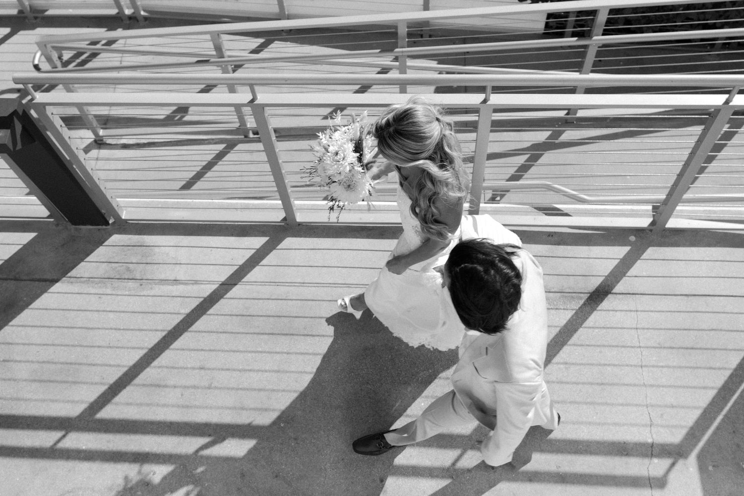 A high angle black and white shot shows two figures dancing on a wooden floor under industrial lighting.