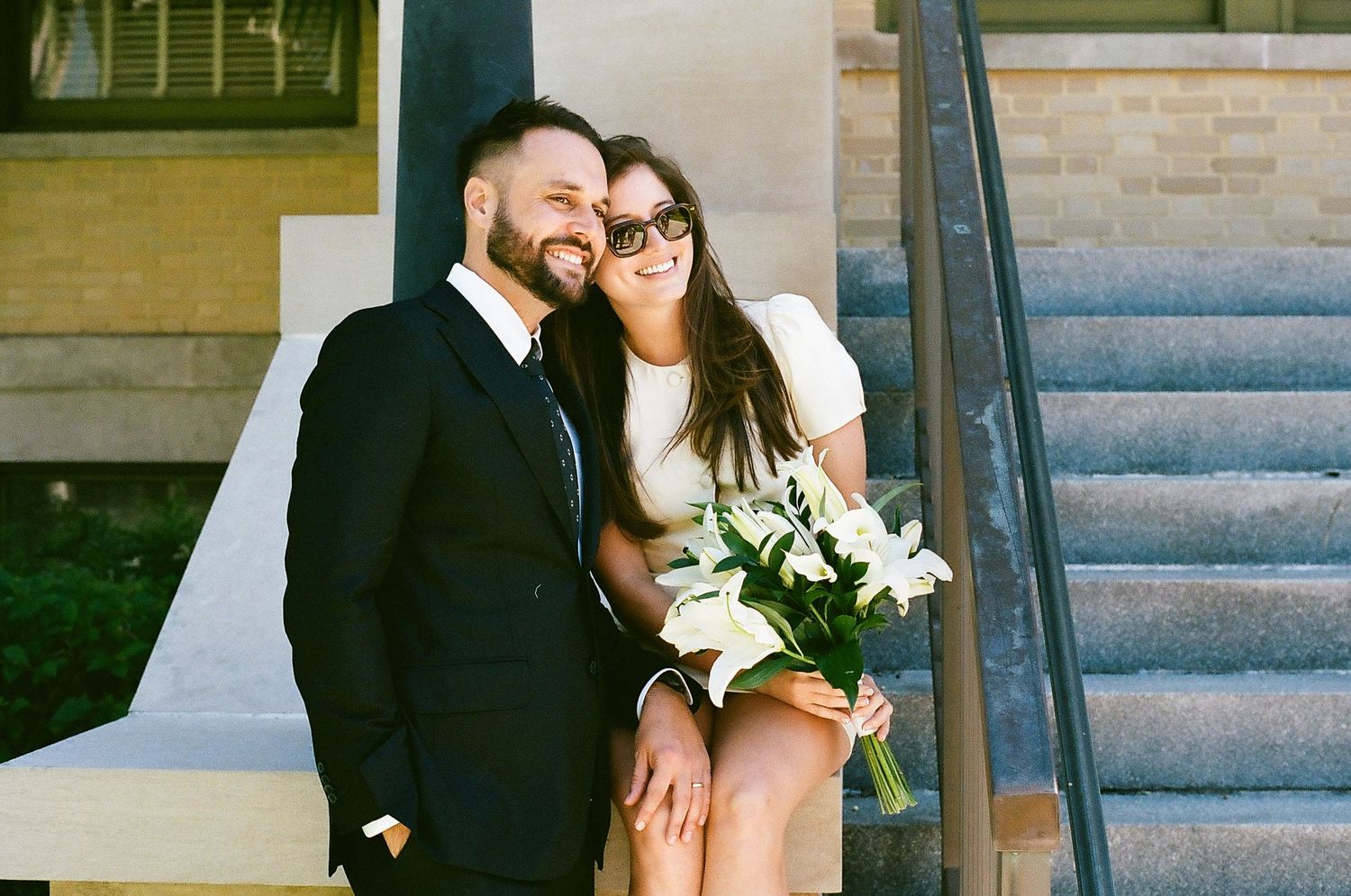 Romantic wedding couple shares intimate moments on stone steps of historic building in elegant formal attire.