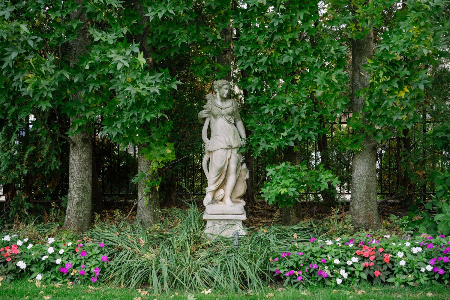 Garden path lined with lush greenery and colorful flowers leads to decorative stone statues.