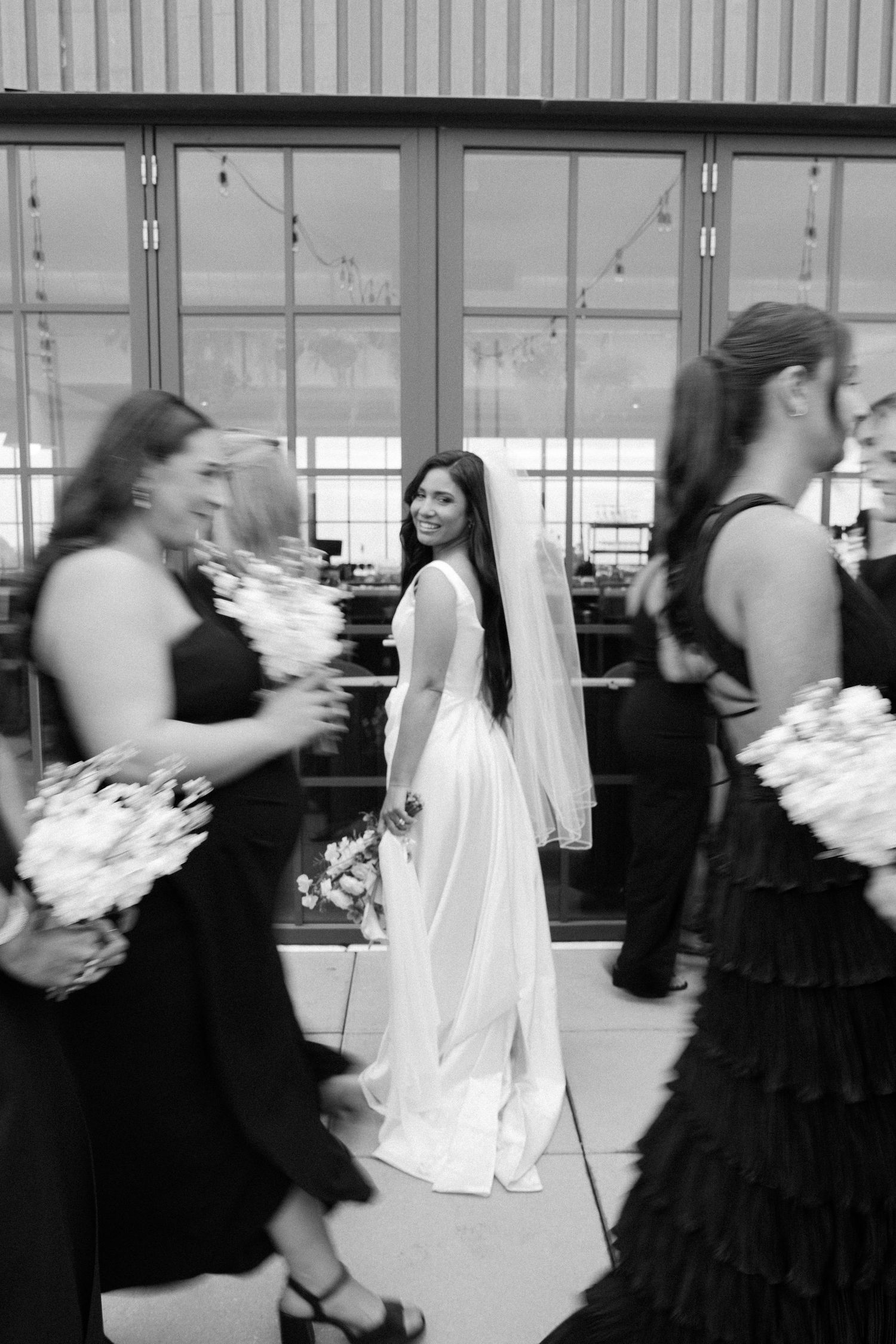 Motion blur of wedding party members in black and white dresses walking through a venue.