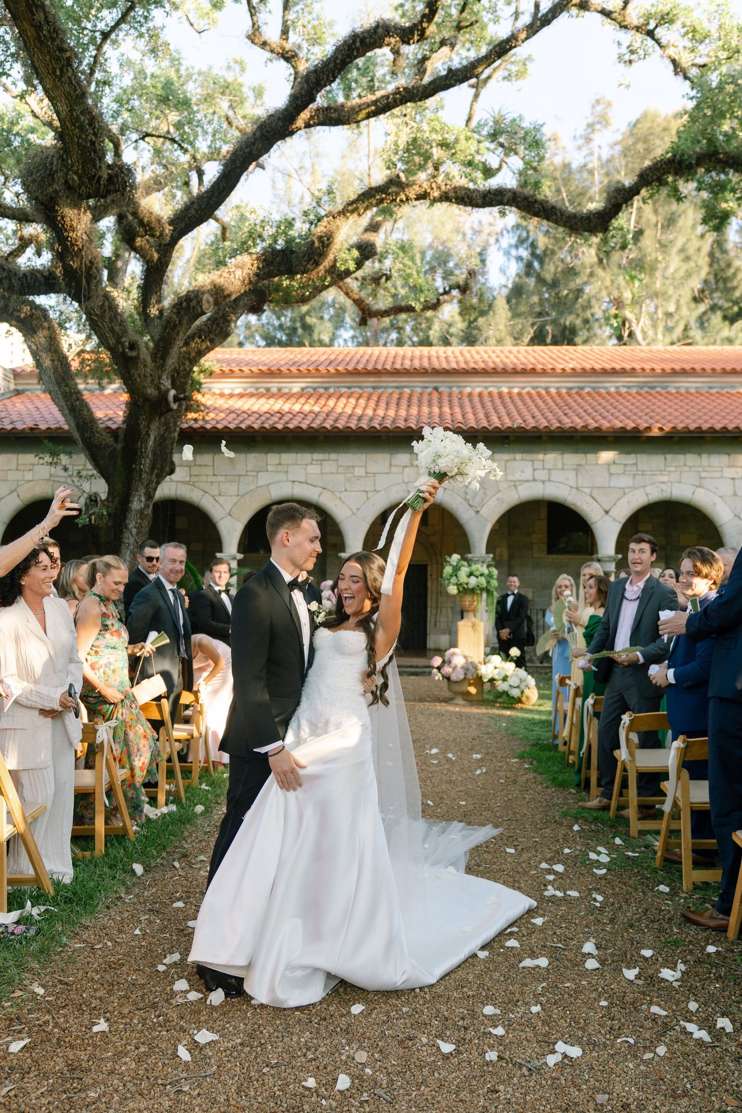 Newlyweds celebrate walking back down aisle as guests cheer at outdoor garden wedding.