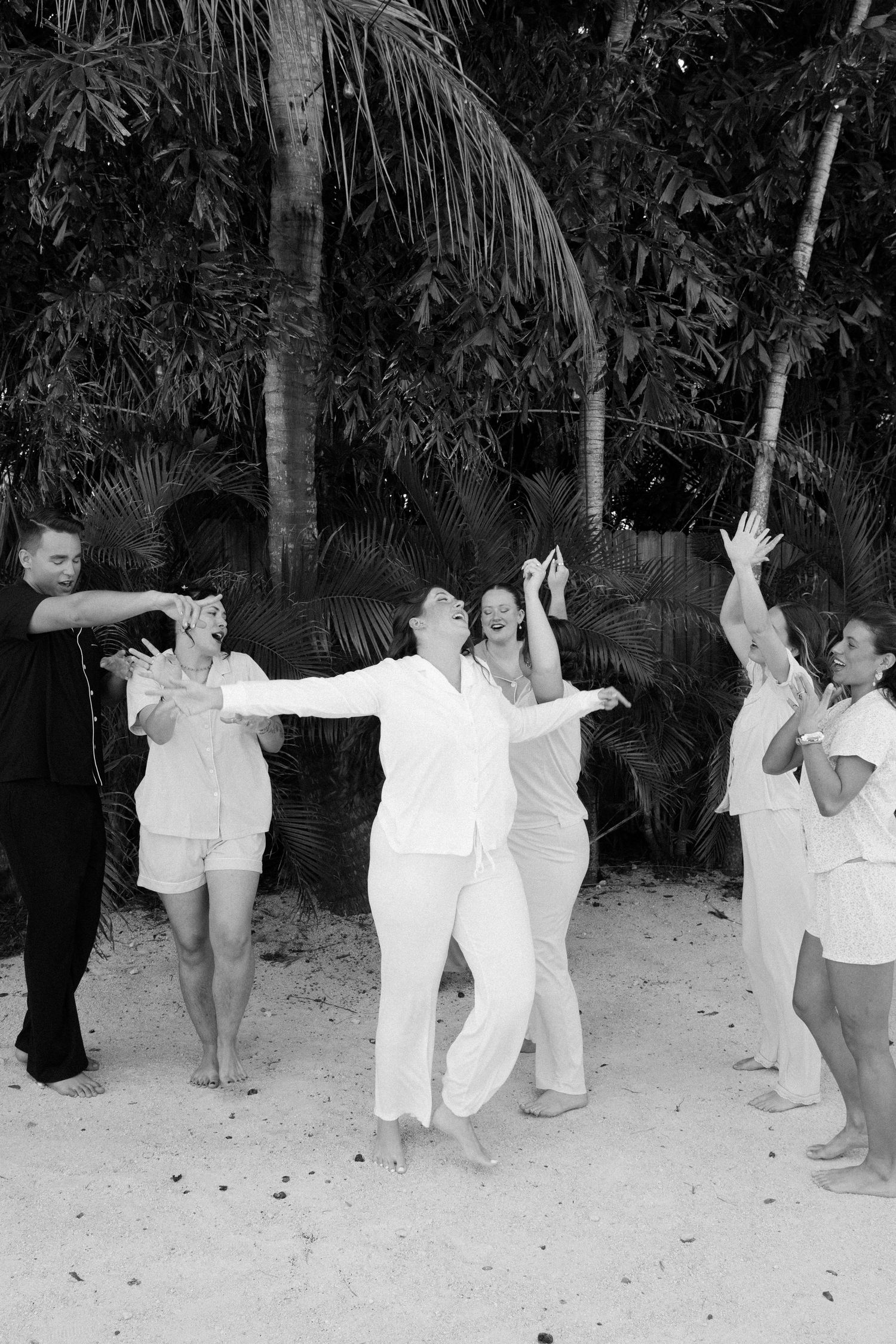 A group of people dancing in a tropical outdoor setting with palm trees.