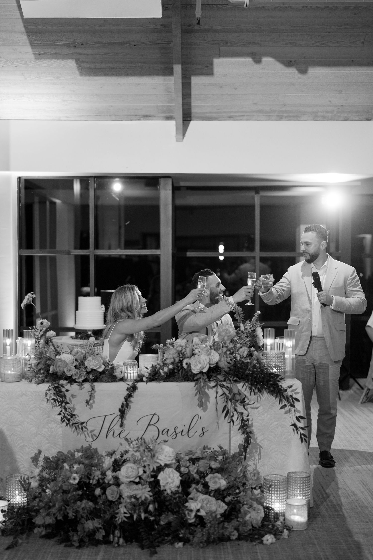 A black and white reception photo showing a toast at a beautifully decorated sweetheart table.