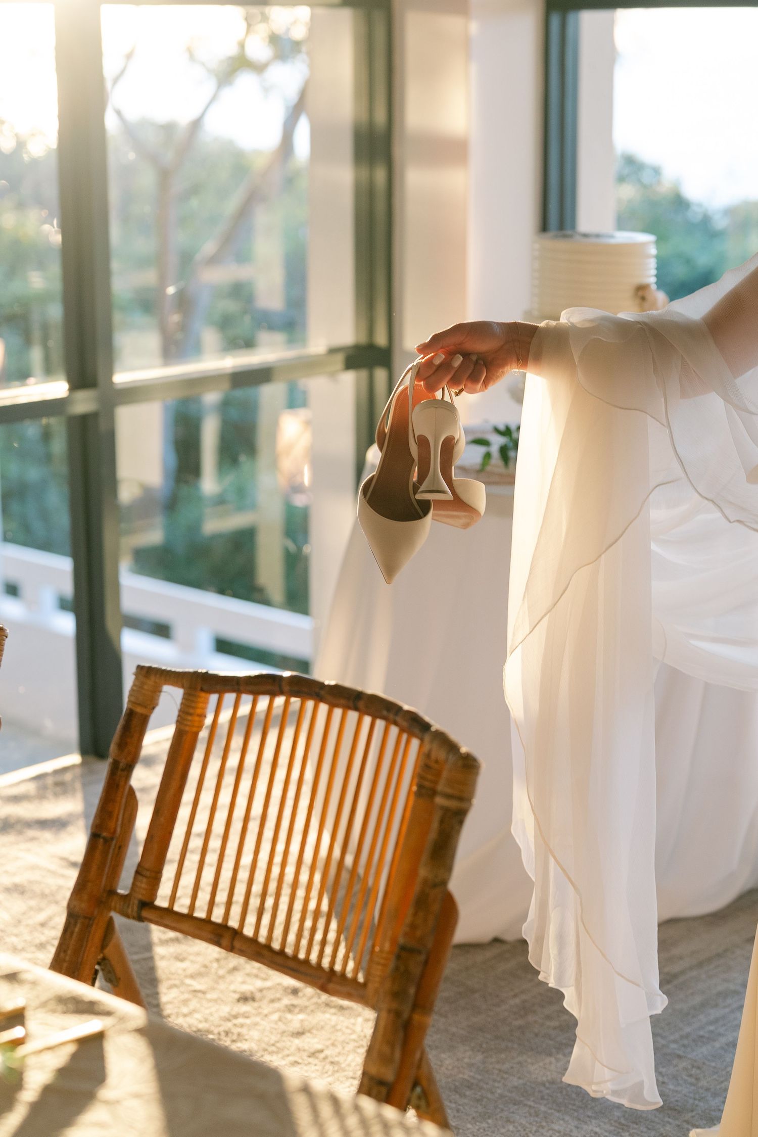 Flowing white wedding dress fabric and wooden benches create an ethereal scene in a sunlit glass-enclosed venue.