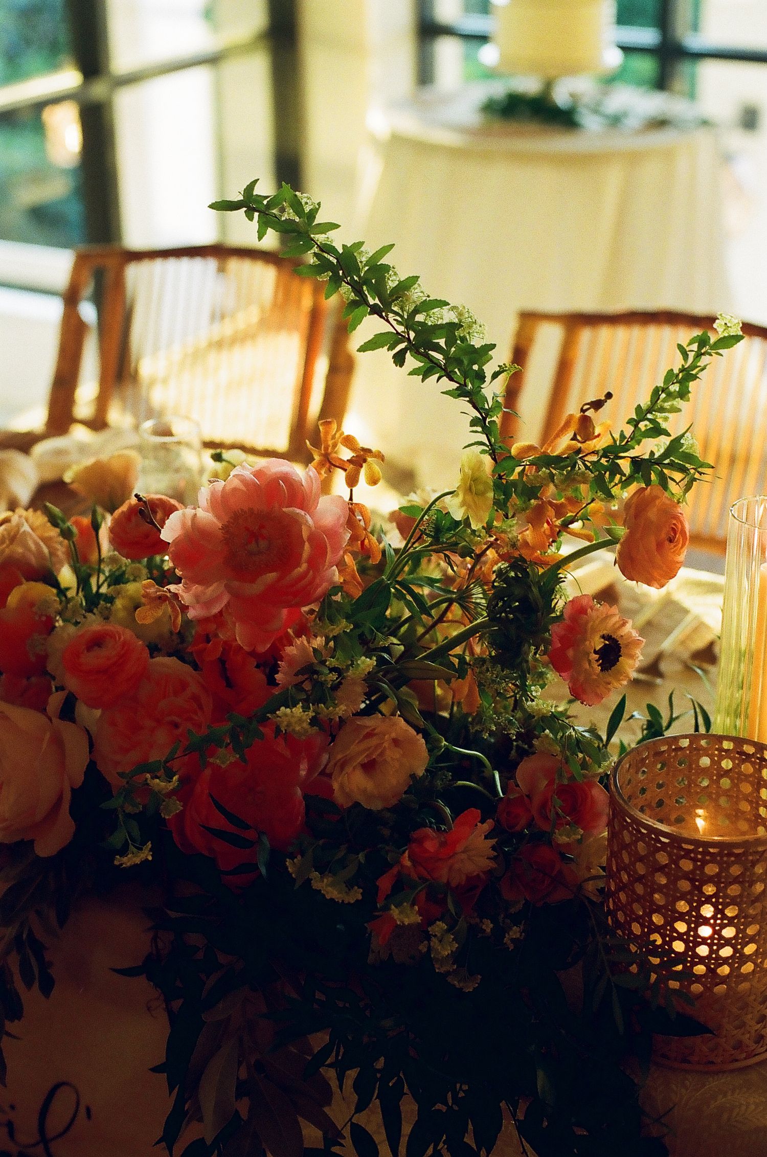 Romantic floral centerpiece with coral roses and greenery alongside candlelight at an evening wedding reception.