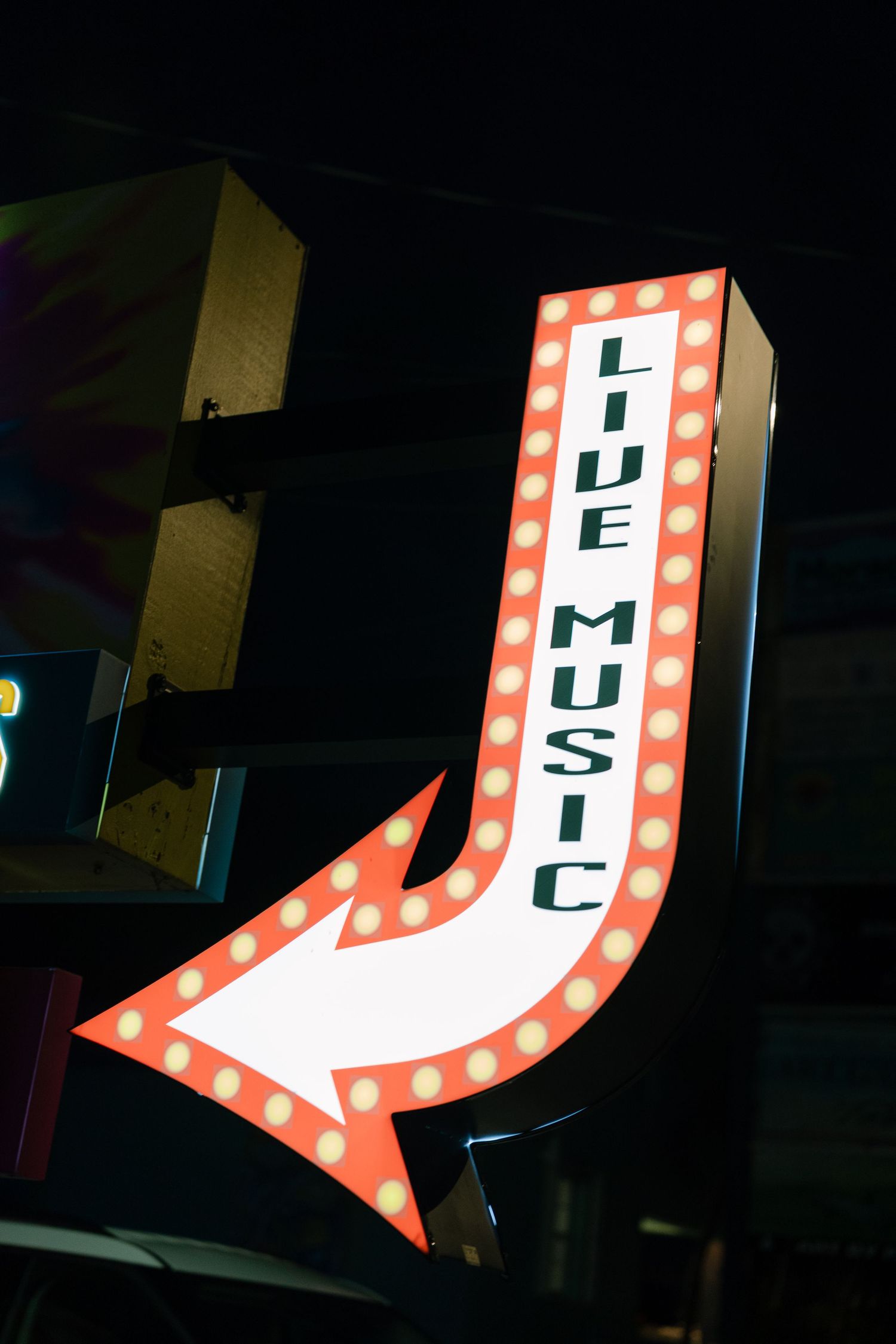 Illuminated retro arrow sign for live music with red lights against dark night sky.
