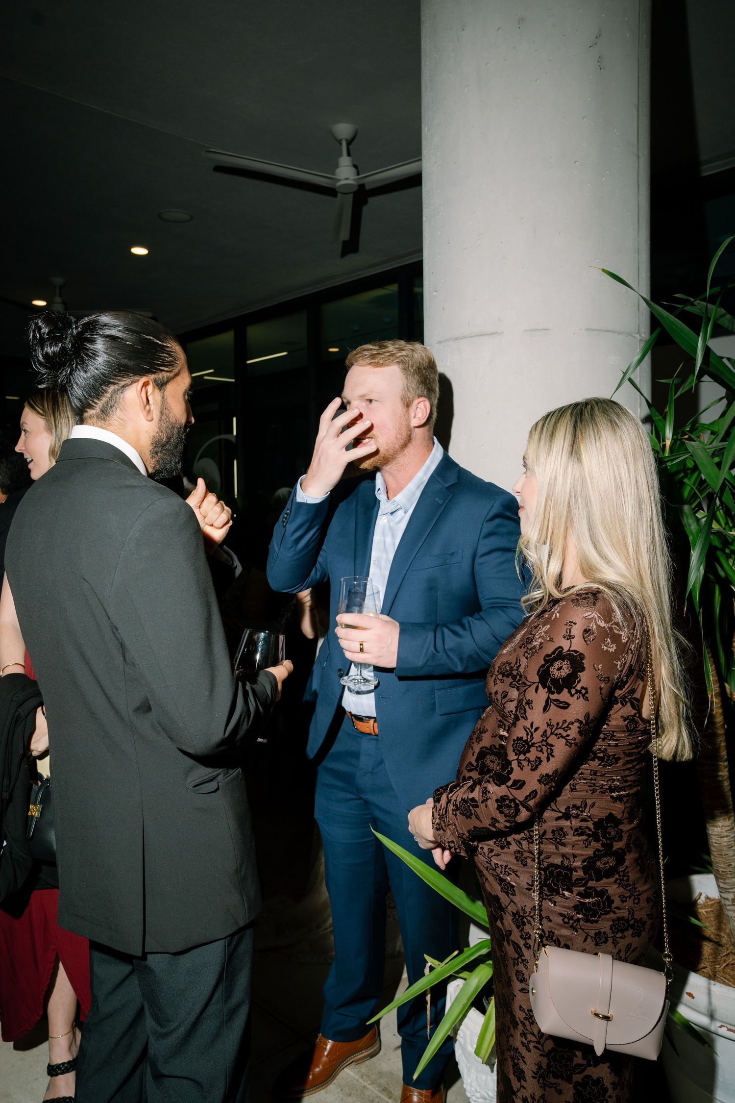 Candid party scene with guests mingling in a modern indoor space with plants.