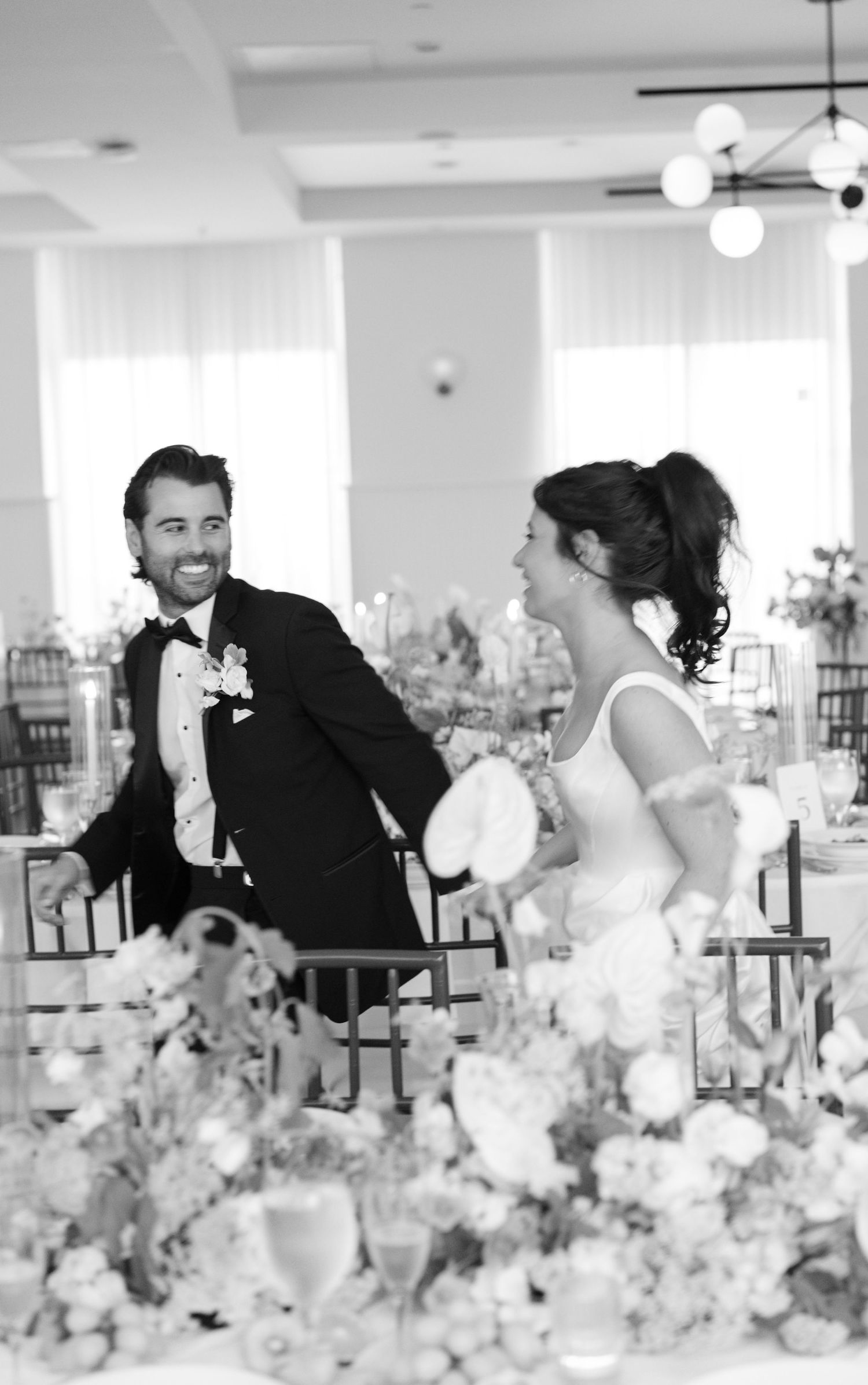 Romantic couple sharing a playful moment behind floral table decorations at their wedding reception.