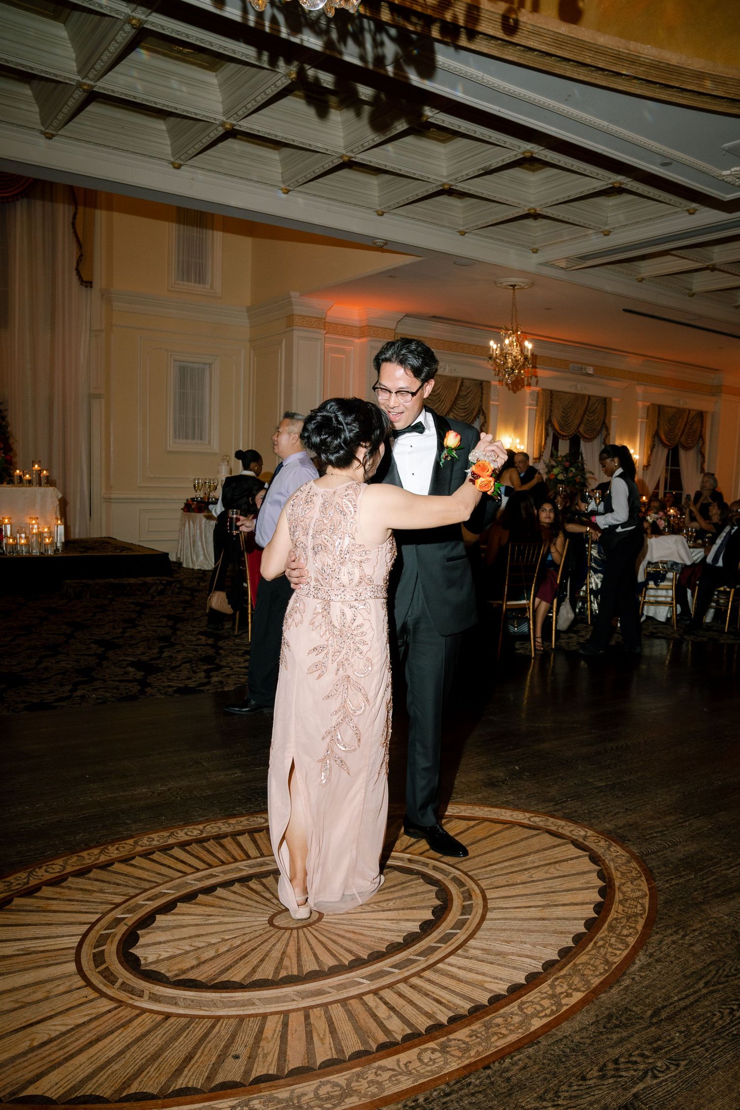 A couple dancing together on an ornate circular patterned ballroom floor at an elegant reception venue.