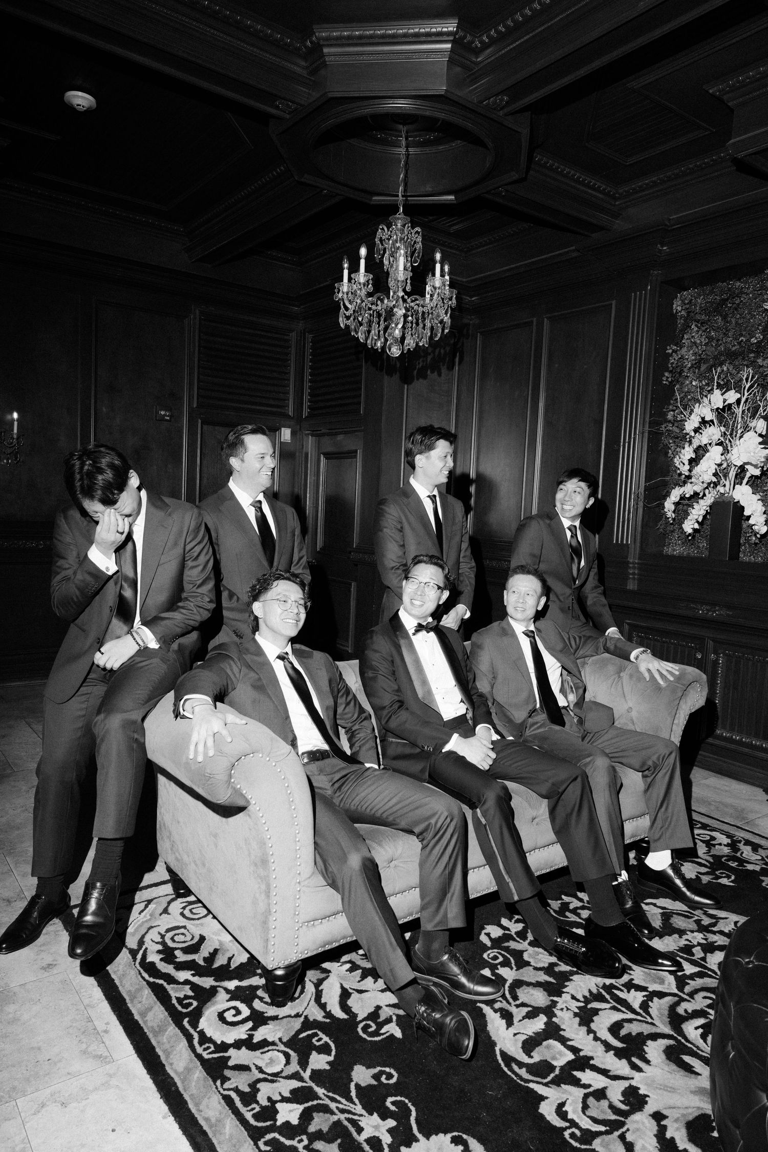 A sequence of black and white photos showing people seated on a patterned couch in an elegant room with chandeliers.