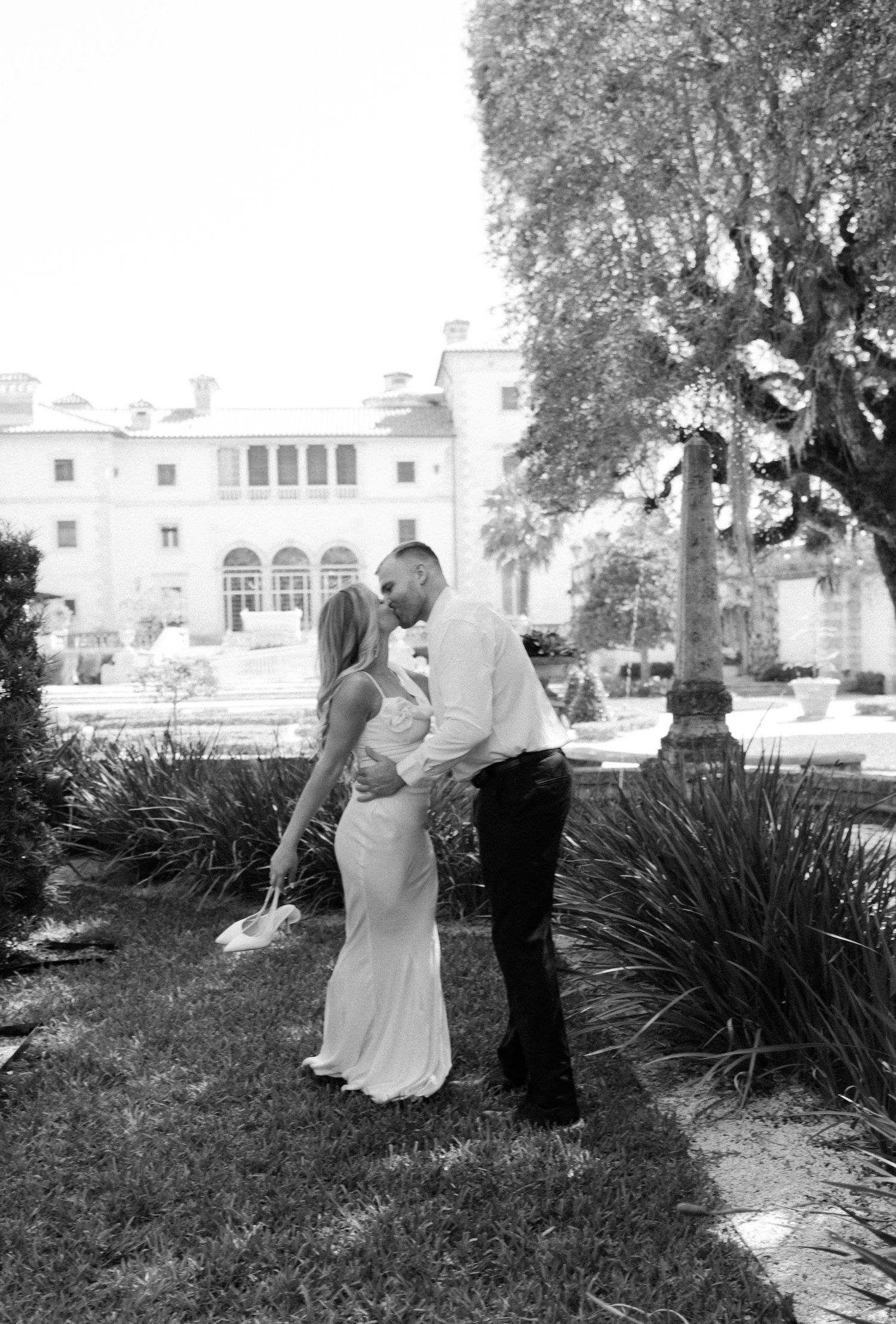 A black and white photo series showing a couple dancing together in a garden setting with white buildings in the background.
