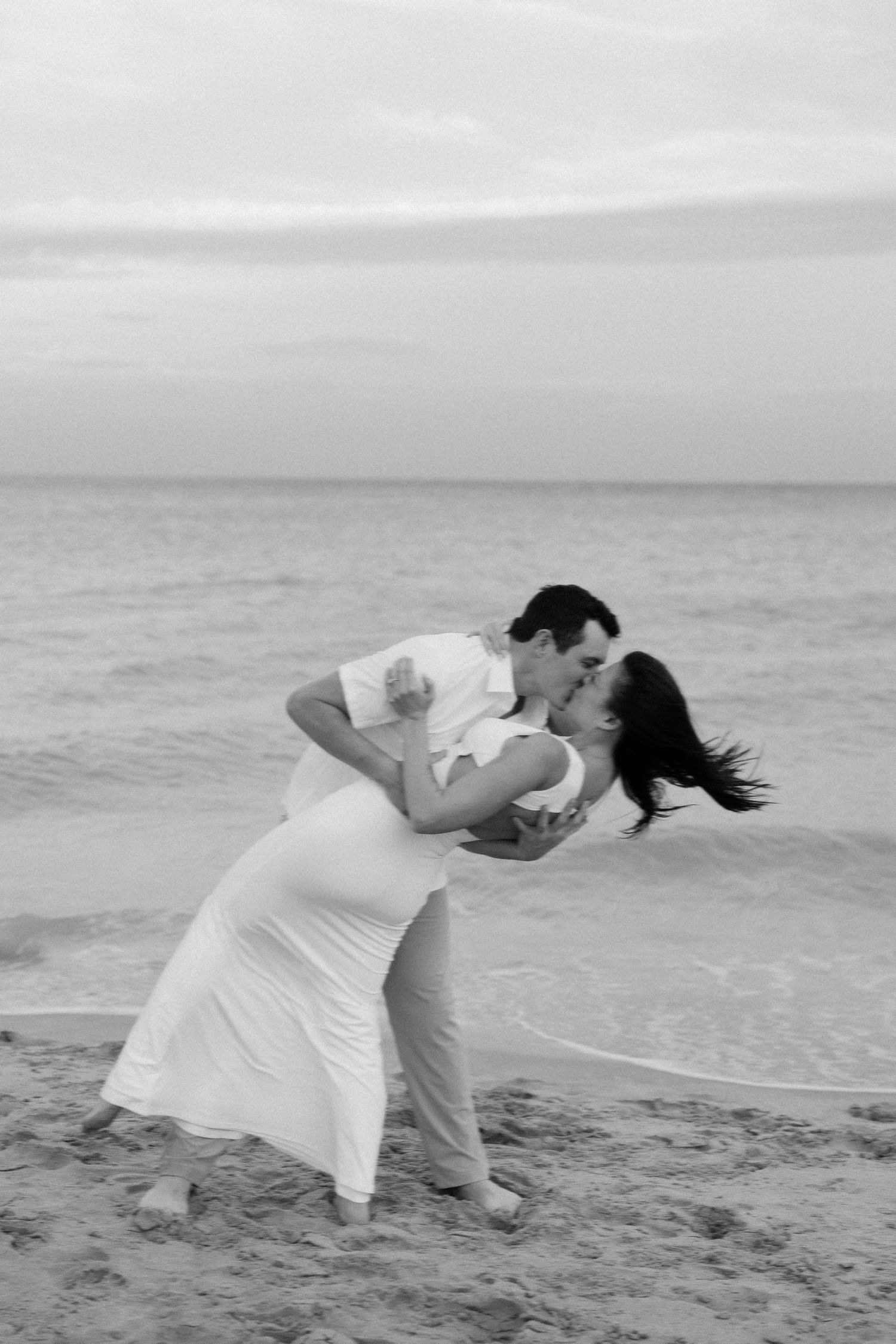 Black and white photo of a couple doing a romantic dip dance pose on the beach.