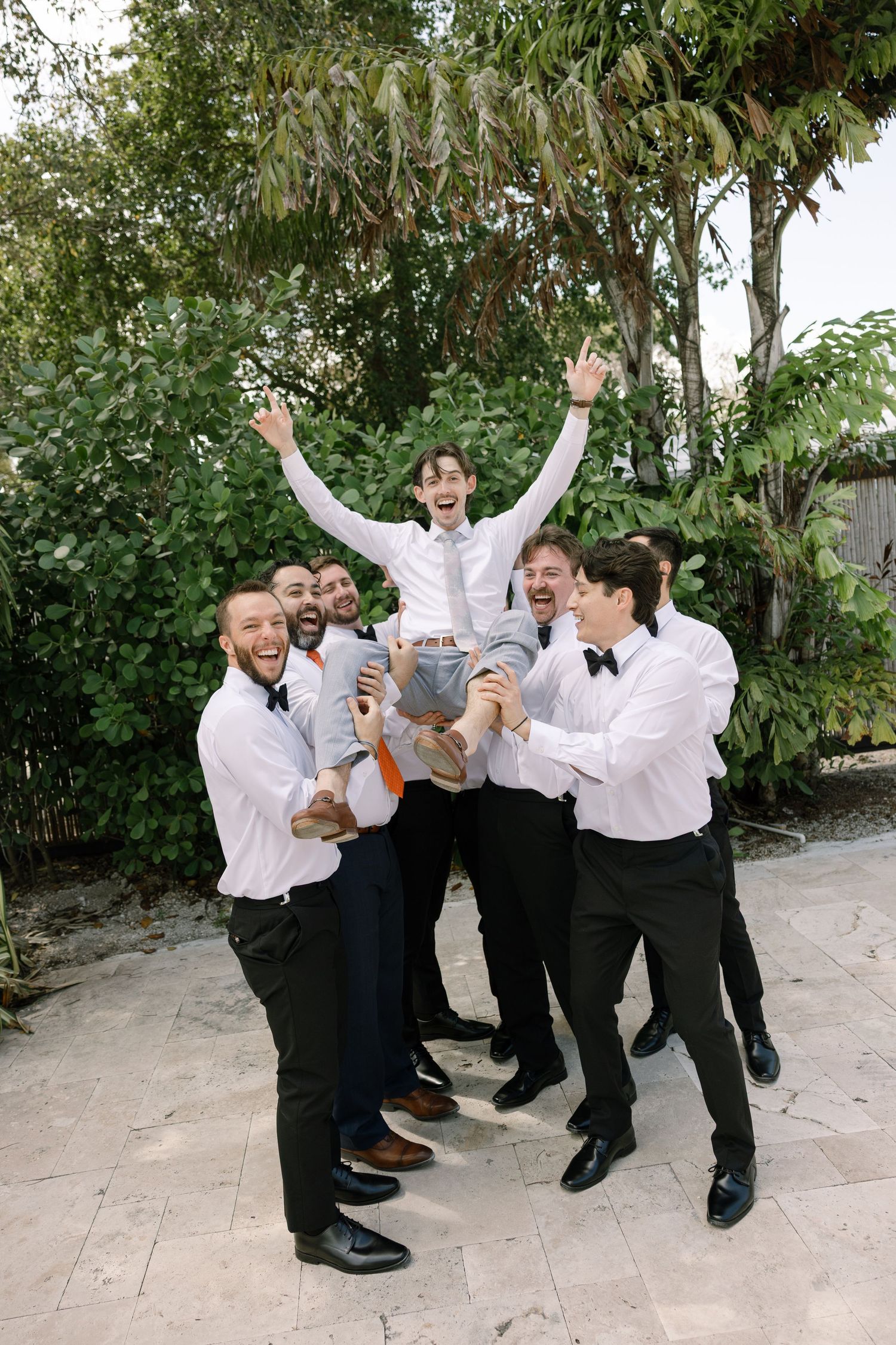 A group of men in formal attire celebrate and raise their hands in a joyful pose.