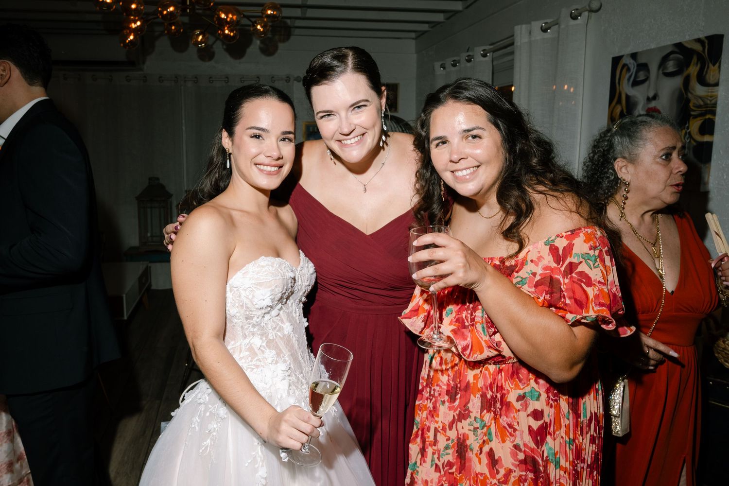 Bride in white strapless gown poses with two guests in red attire at elegant wedding reception.