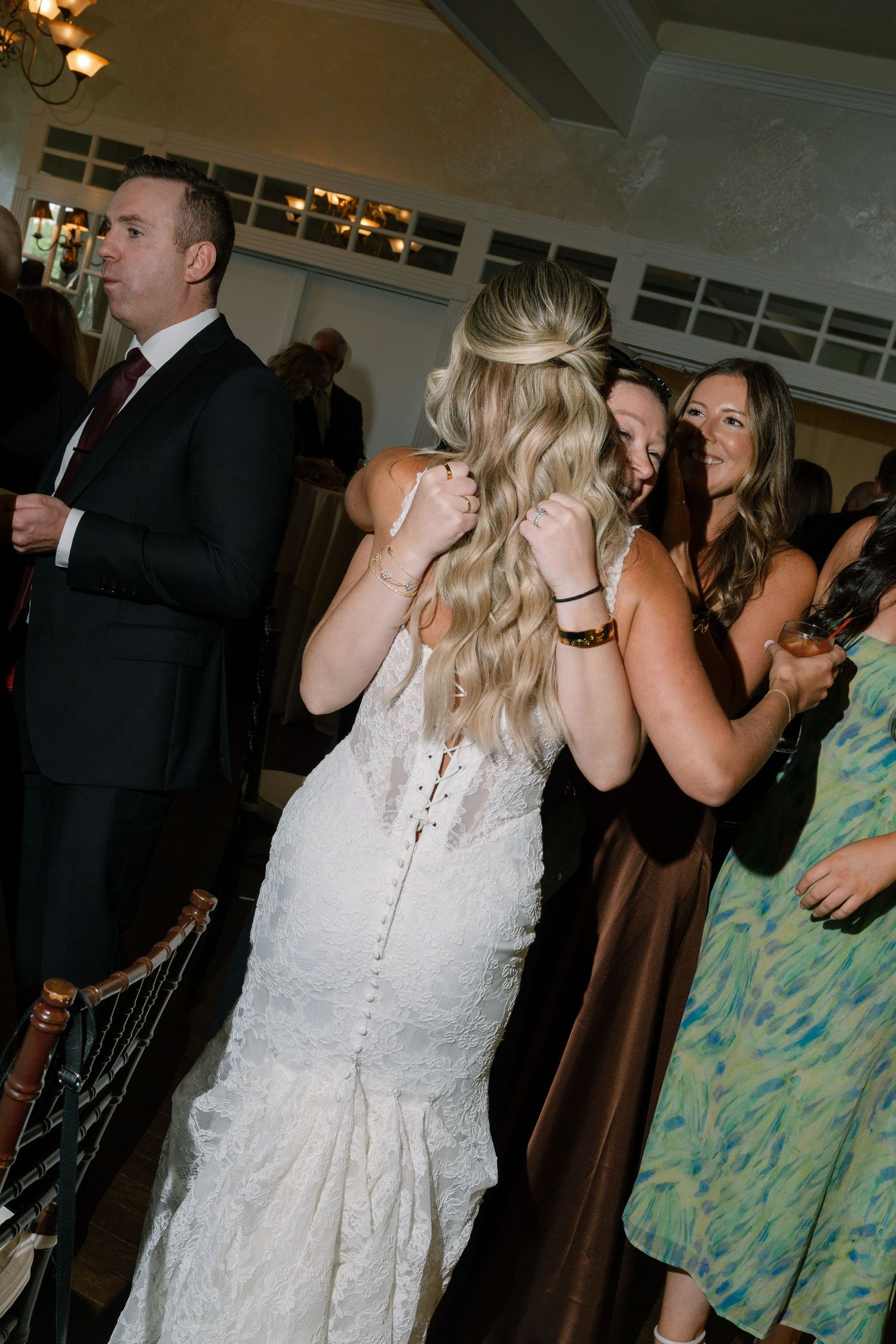 Bride in lace mermaid gown shares an emotional hug with a guest on the dance floor.