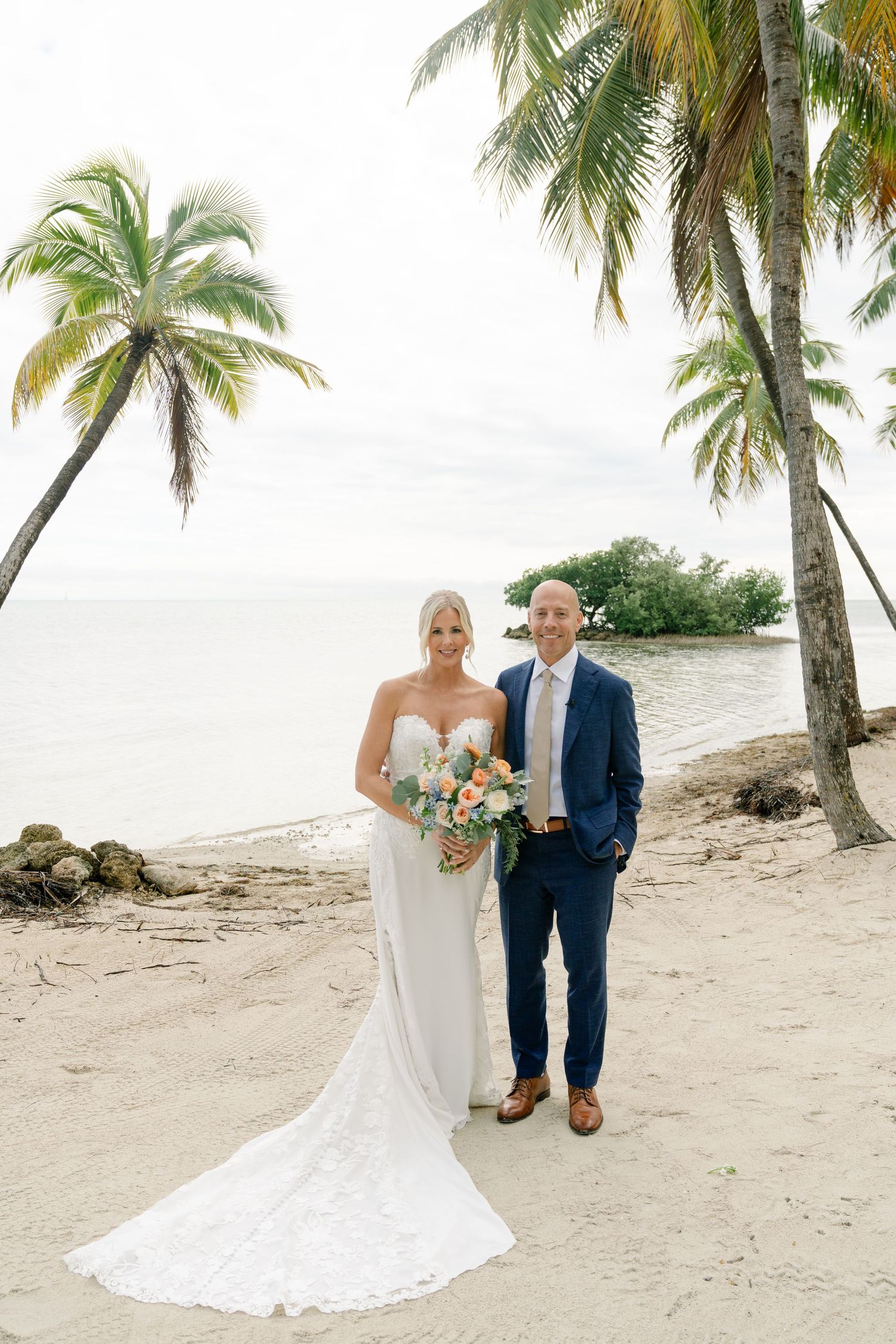 Newlyweds walking along a tropical beach with palm trees and ocean views.