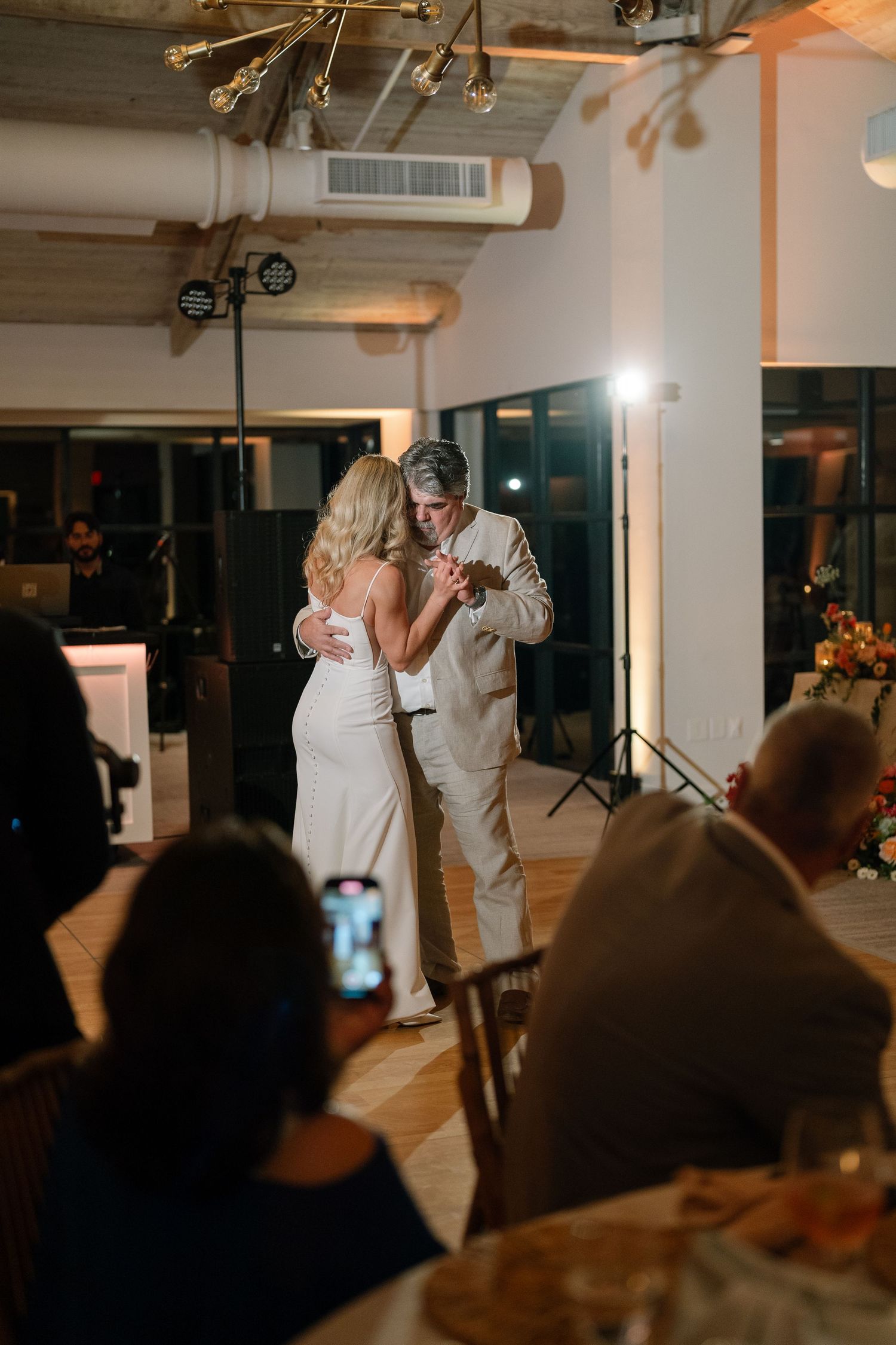 Wedding guests watching a couple's first dance at an indoor reception with dramatic lighting.