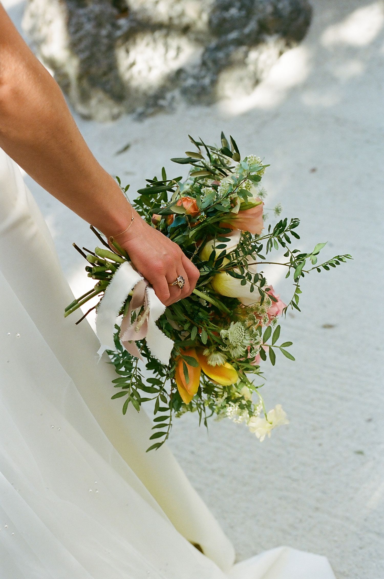 Wedding bouquet with green foliage and white flowers being held against a light background.