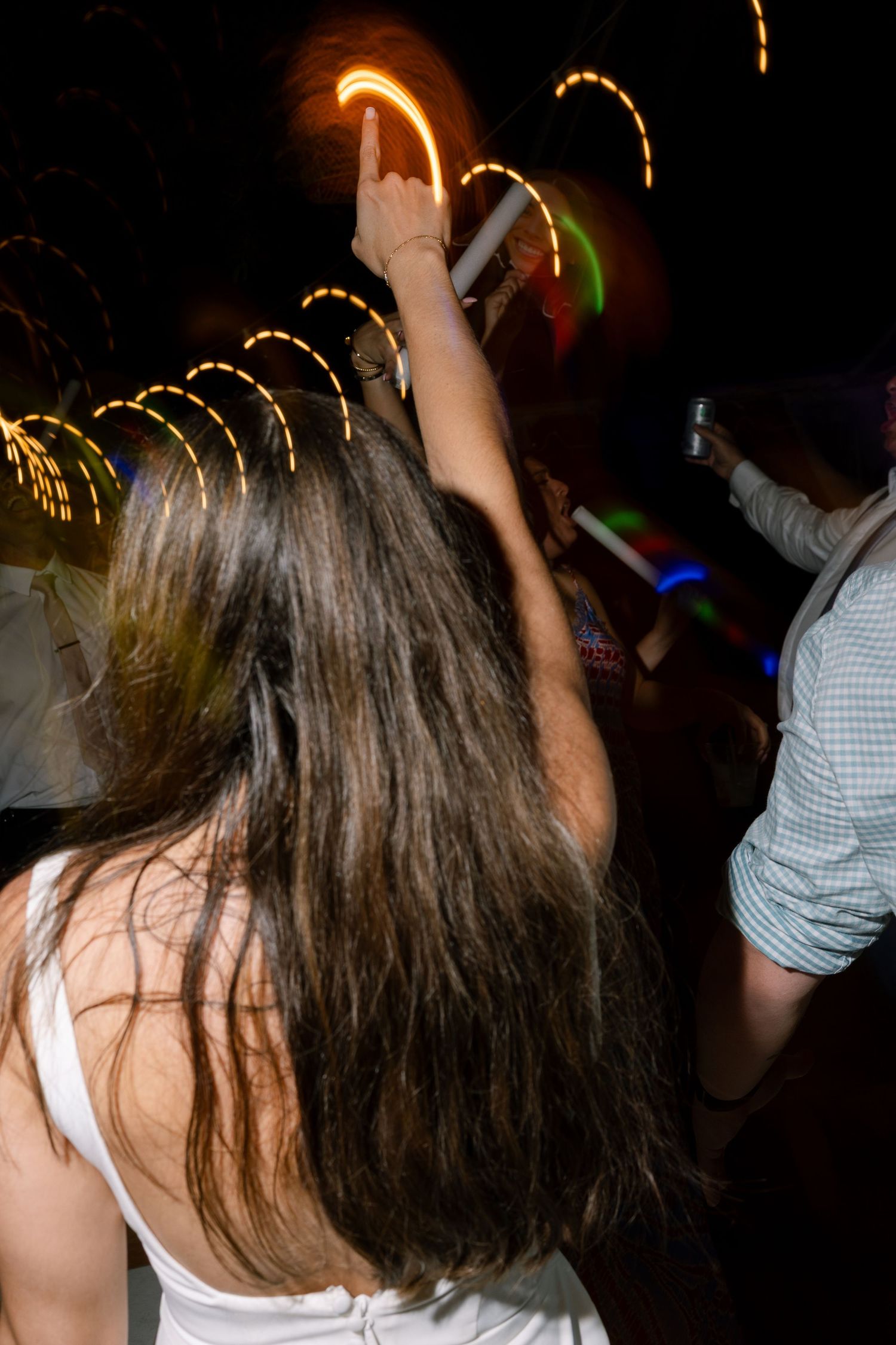Bride dancing with arm raised under colorful light trails at nighttime wedding reception.