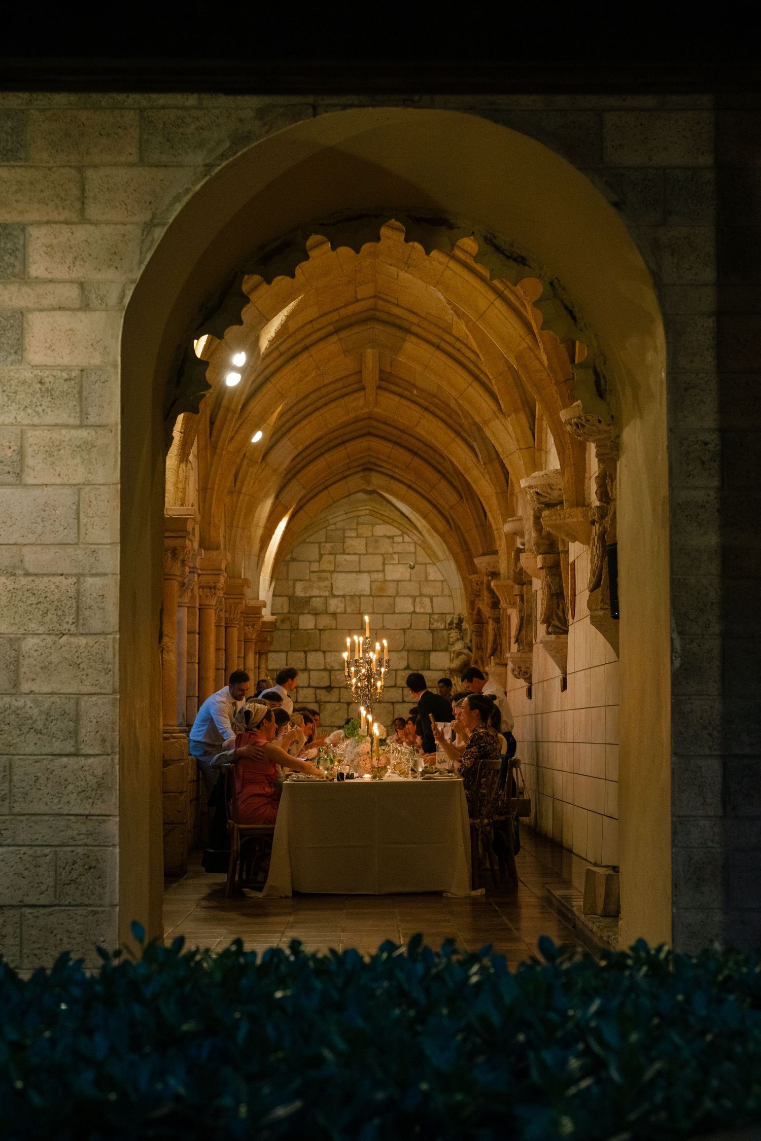 Candlelit dinner in a Gothic stone archway with guests gathered around an elegant table in a medieval setting.