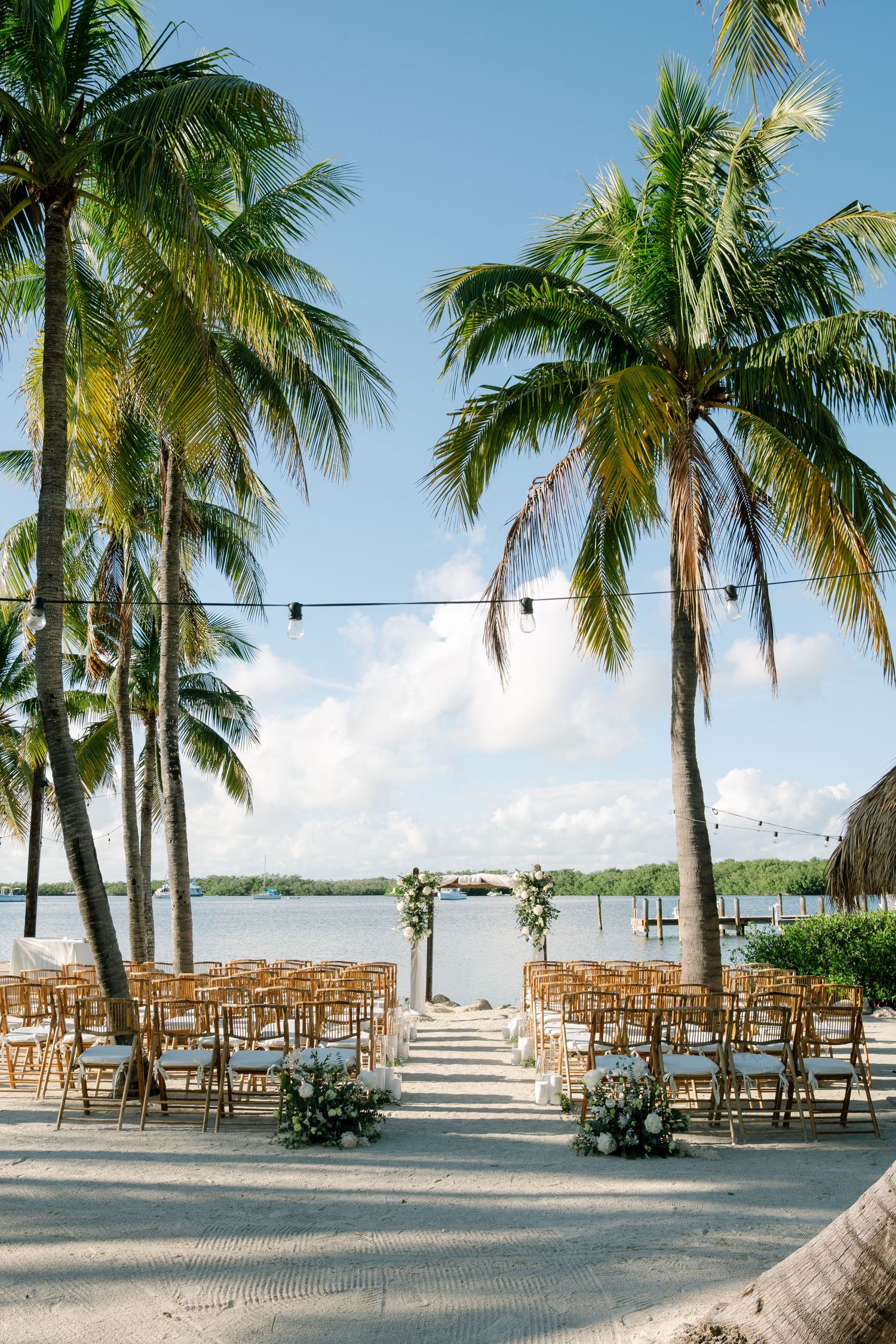 Tropical beach wedding ceremony setup with wooden chairs between palm trees overlooking the ocean in Florida Keys.