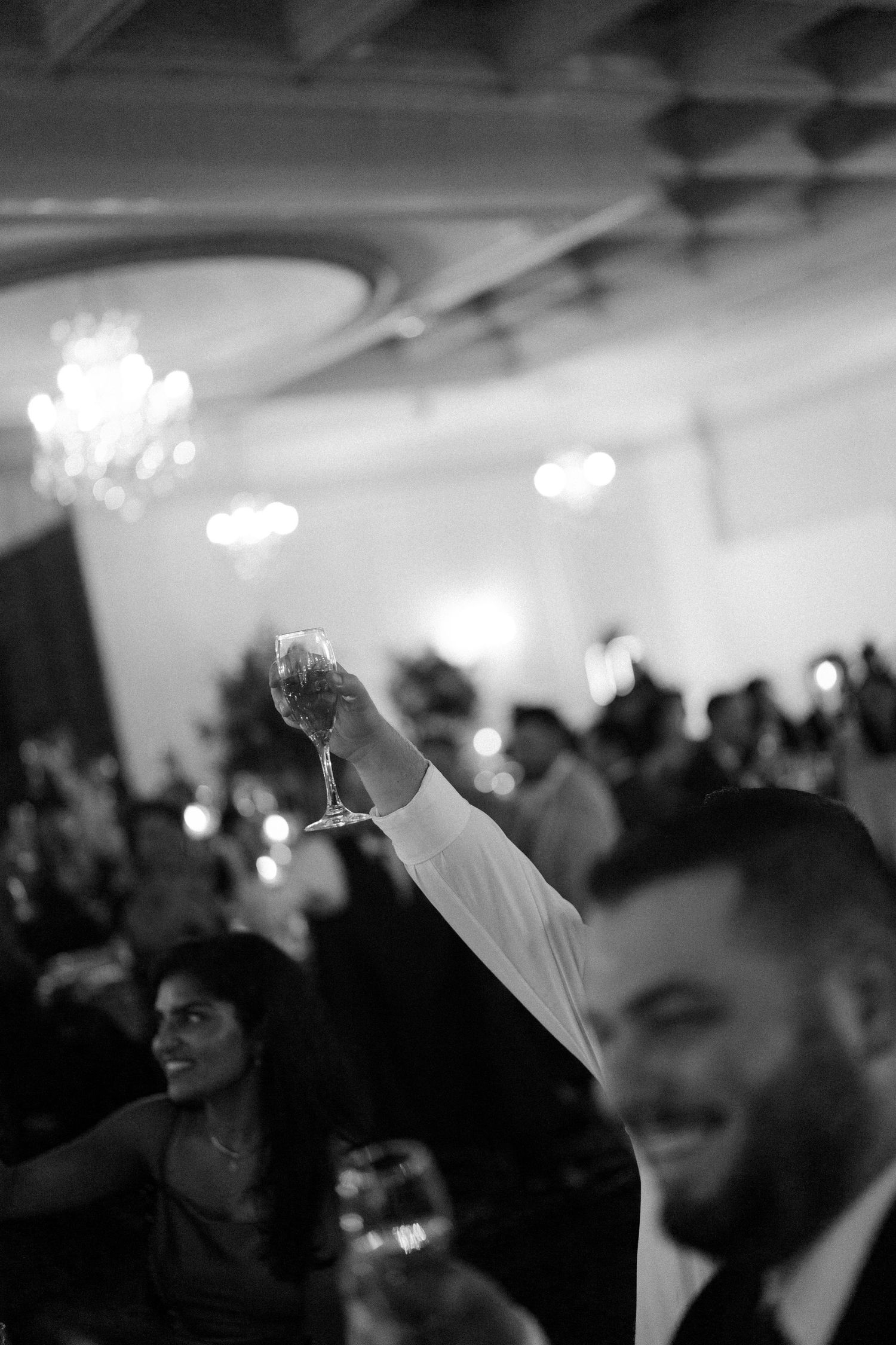 Black and white photo of a wedding reception with guests dancing in a dimly lit ballroom.