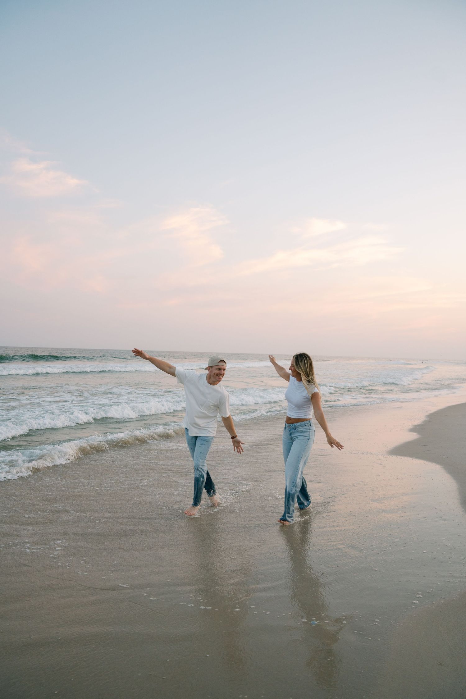 People in blue jeans playing and splashing in the ocean waves at sunset along a peaceful beach shoreline.