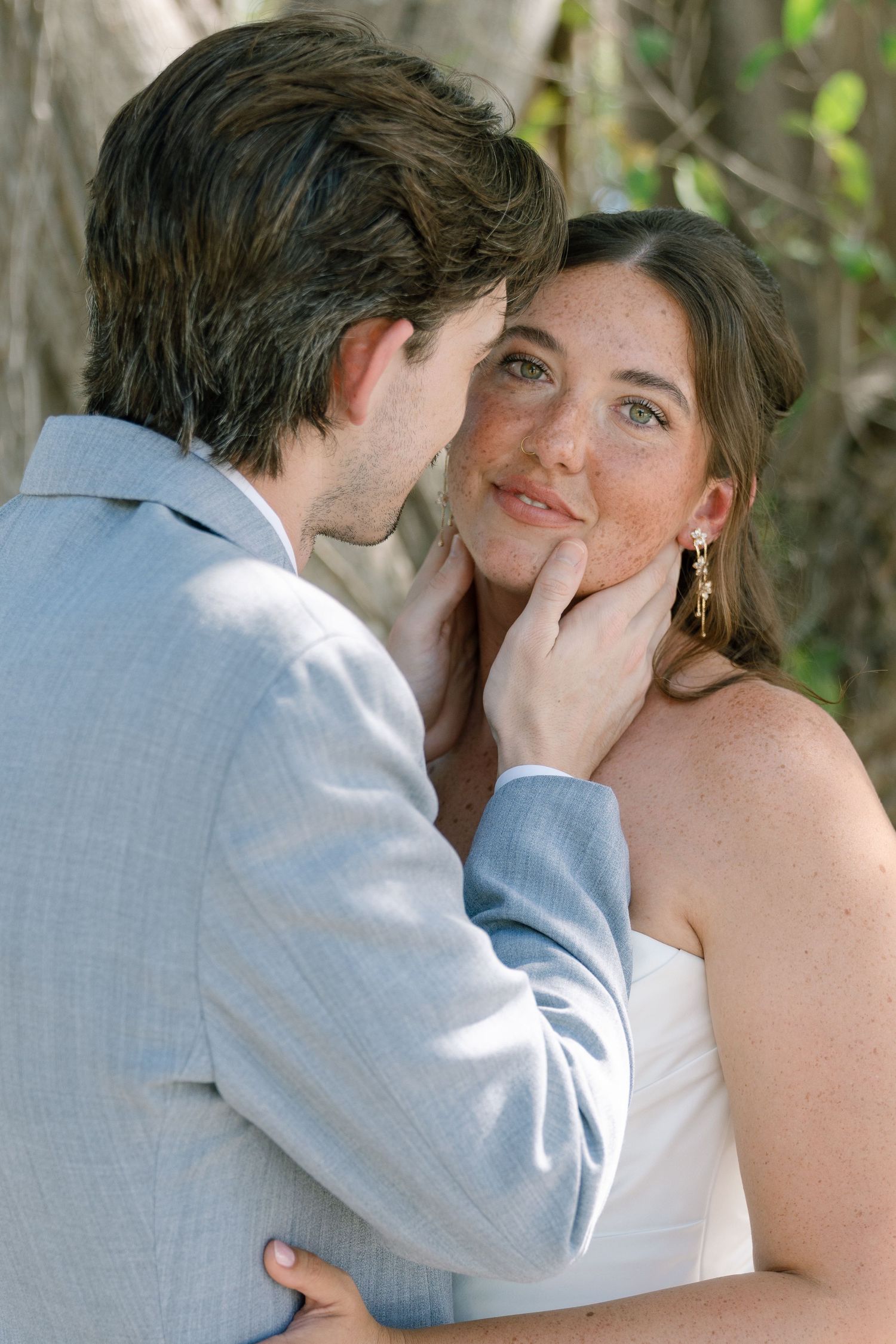 A couple embrace and smile at each other in a tropical setting.