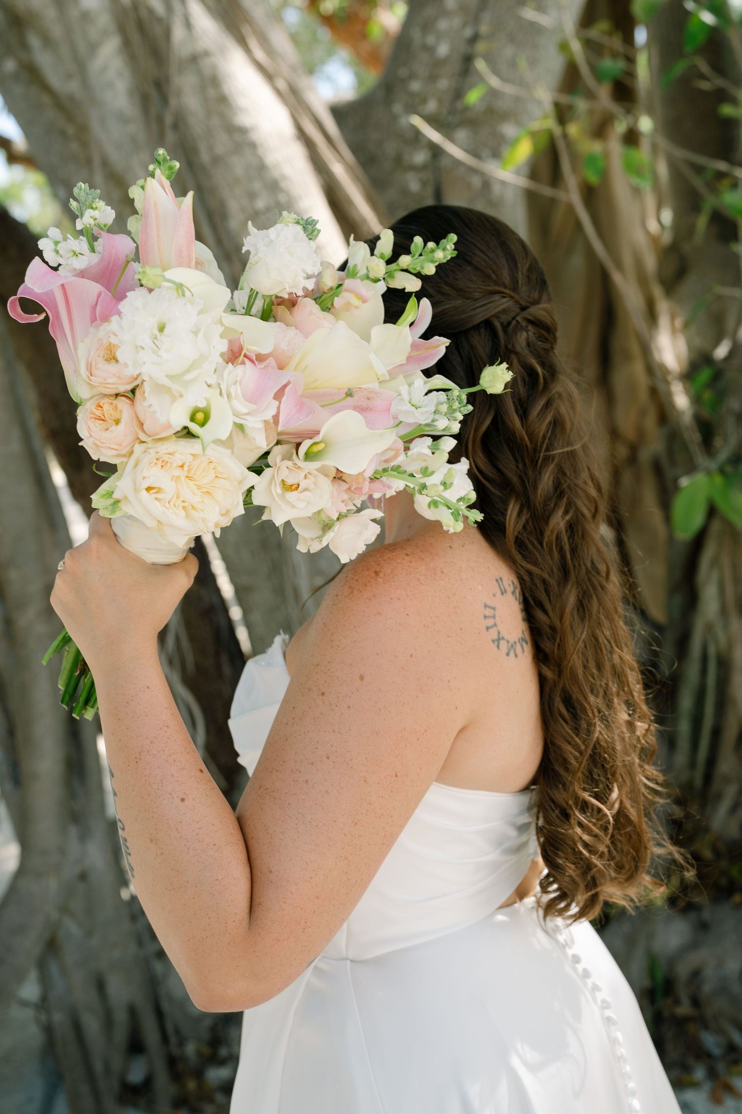 A woman in a white dress holds a bouquet of pink and white flowers in a lush, natural setting.
