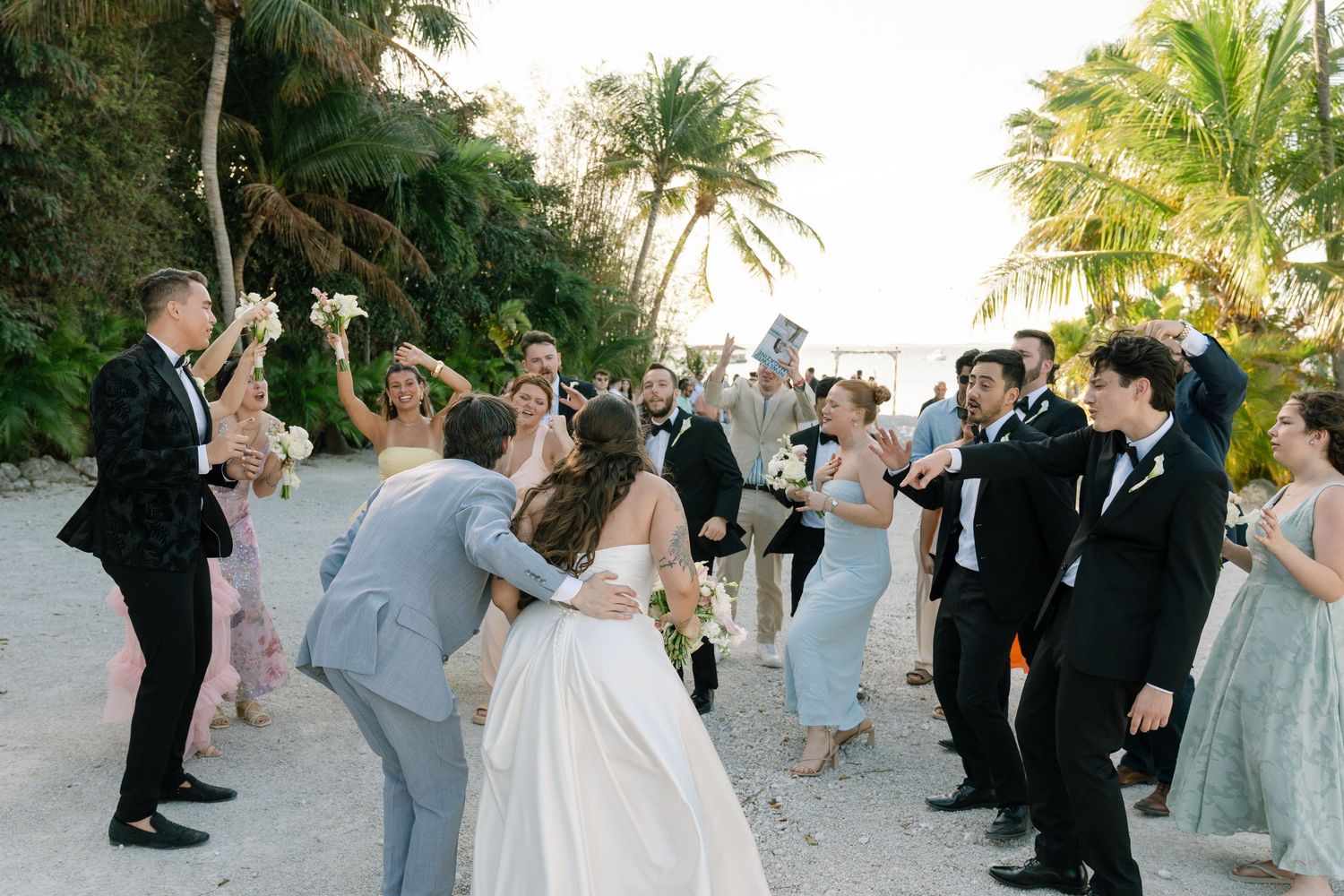 A wedding party gathered on a beach with the bride and groom in the center.
