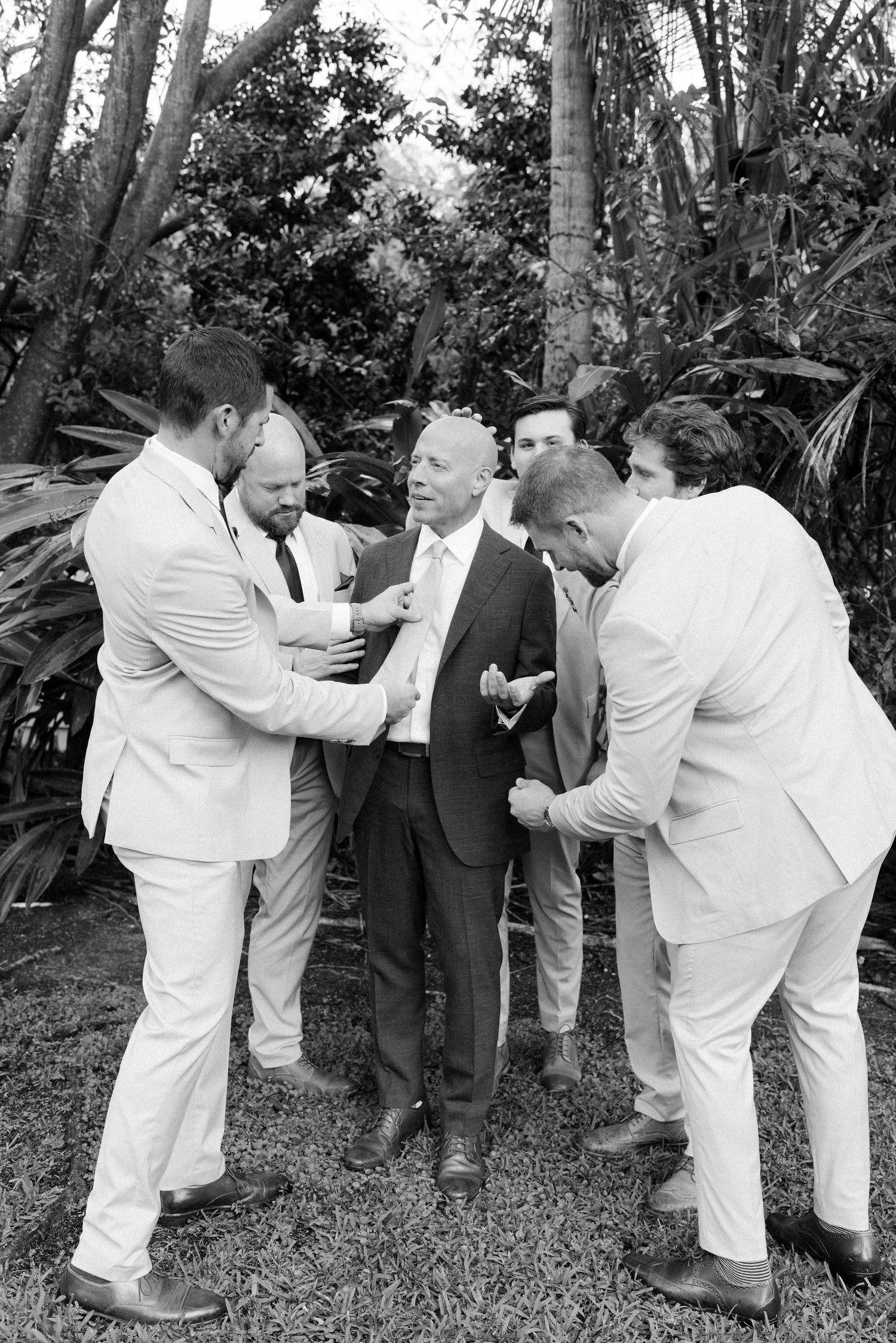 A group of men in light colored suits having an animated discussion outdoors among tropical foliage.