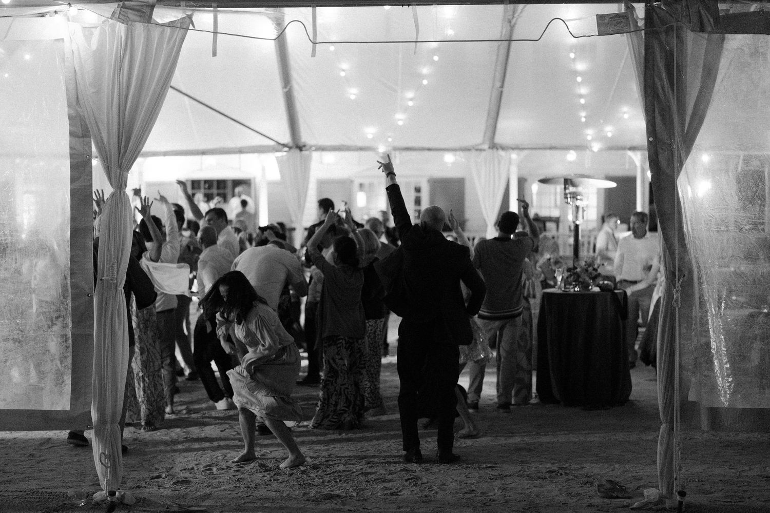 Black and white photo of wedding reception inside an elegant tent with dancing guests.