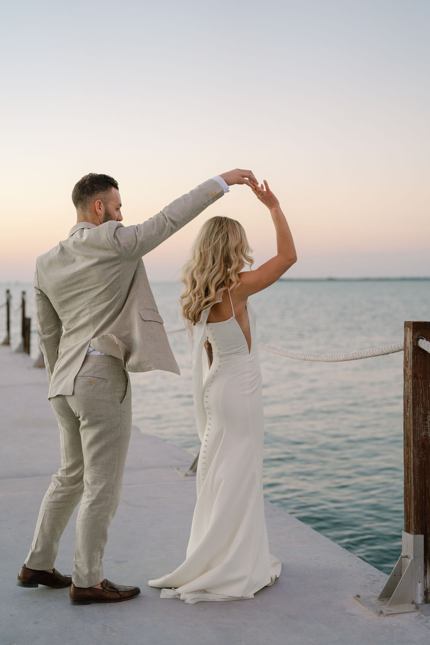 Couple dancing together on a pier at sunset with ocean views.