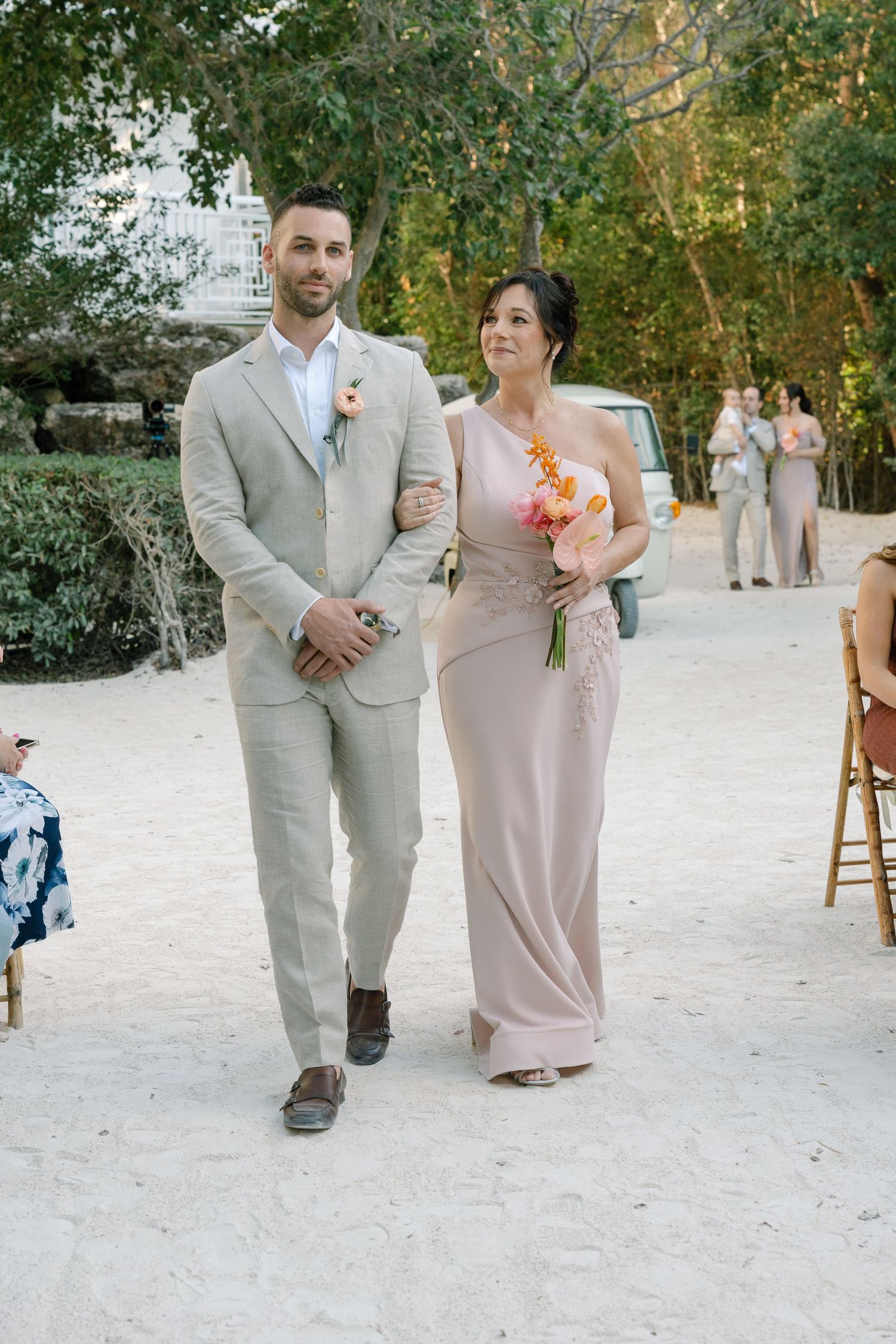 Wedding couple walking together on a white sandy beach path surrounded by tropical trees.
