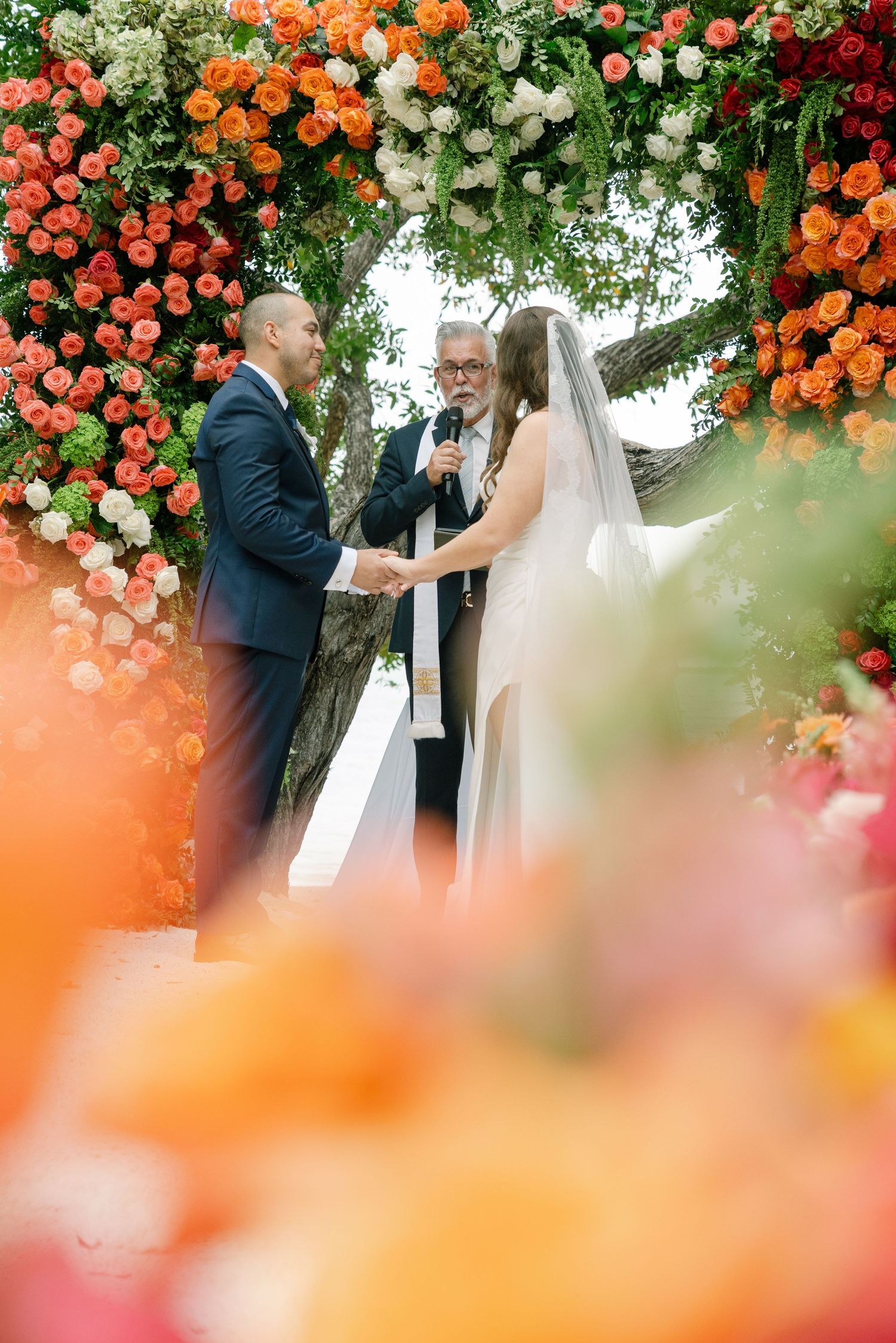 Wedding ceremony under a floral arch with vibrant orange and white blooms framing an intimate outdoor moment.