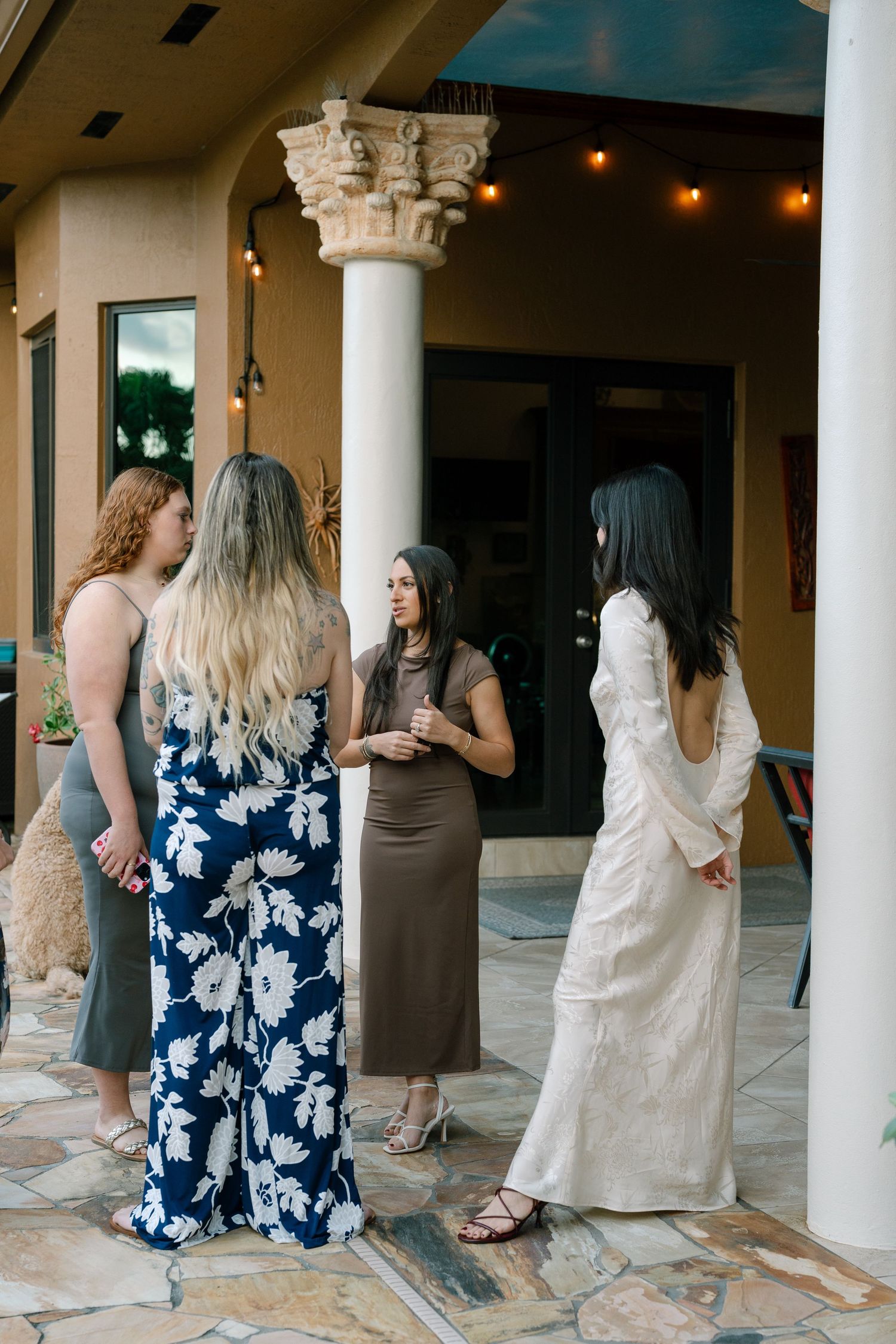 Group gathering on a covered patio with classical columns and floral dresses visible.